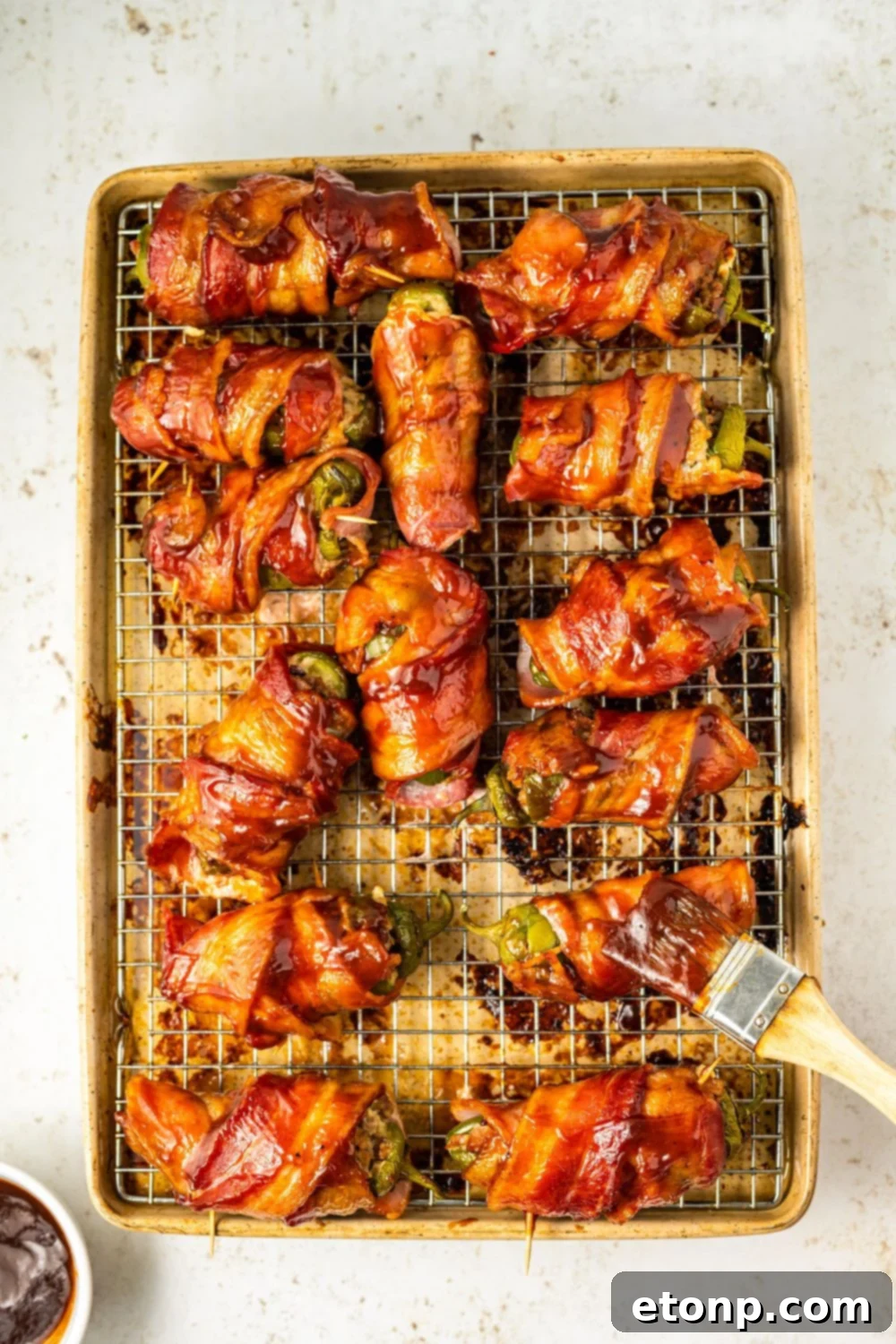 A BBQ brush applying a generous layer of BBQ sauce over the top of Texas Twinkies on a baking sheet