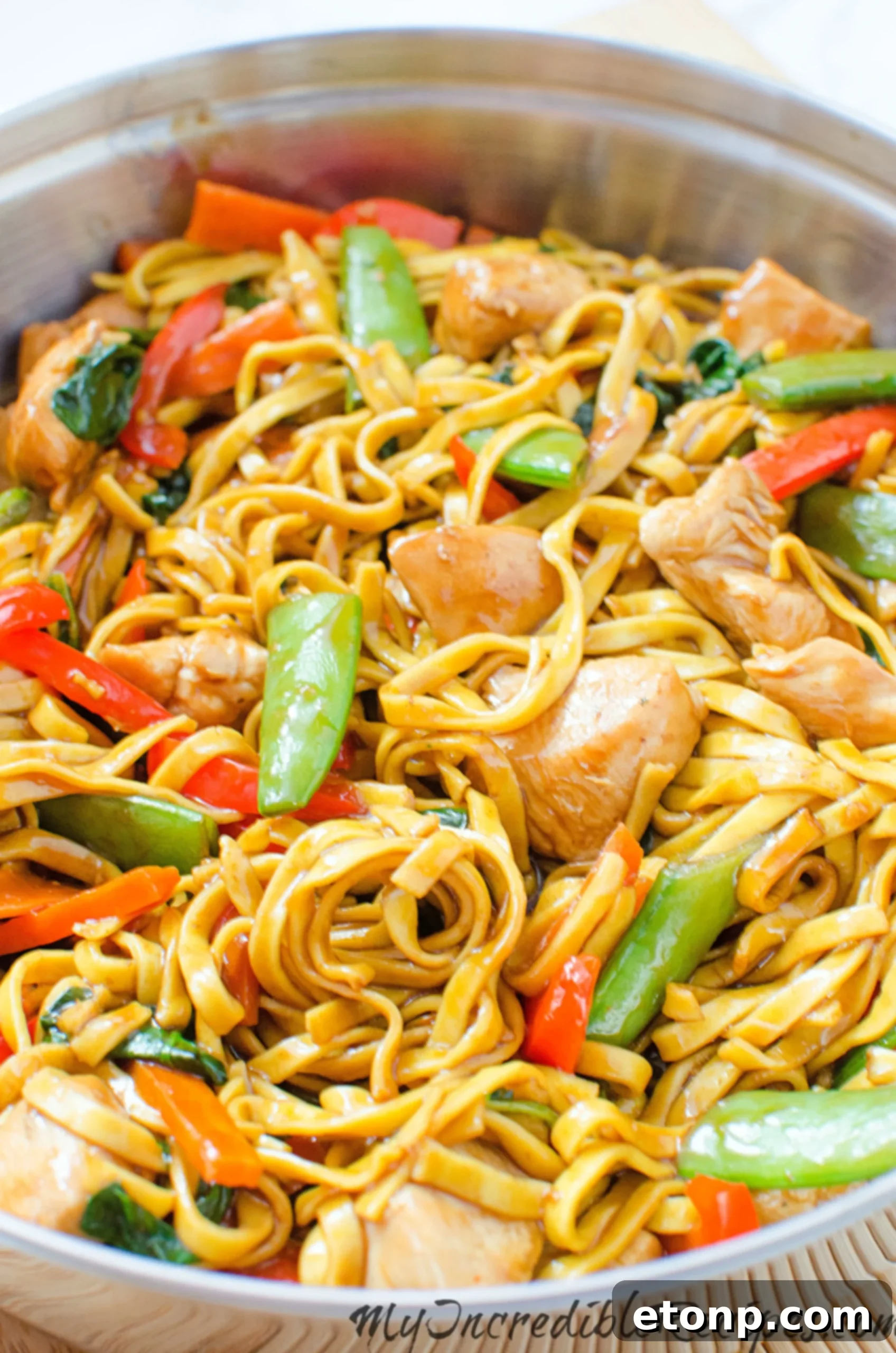 Chicken lo mein being tossed in a pan with tongs
