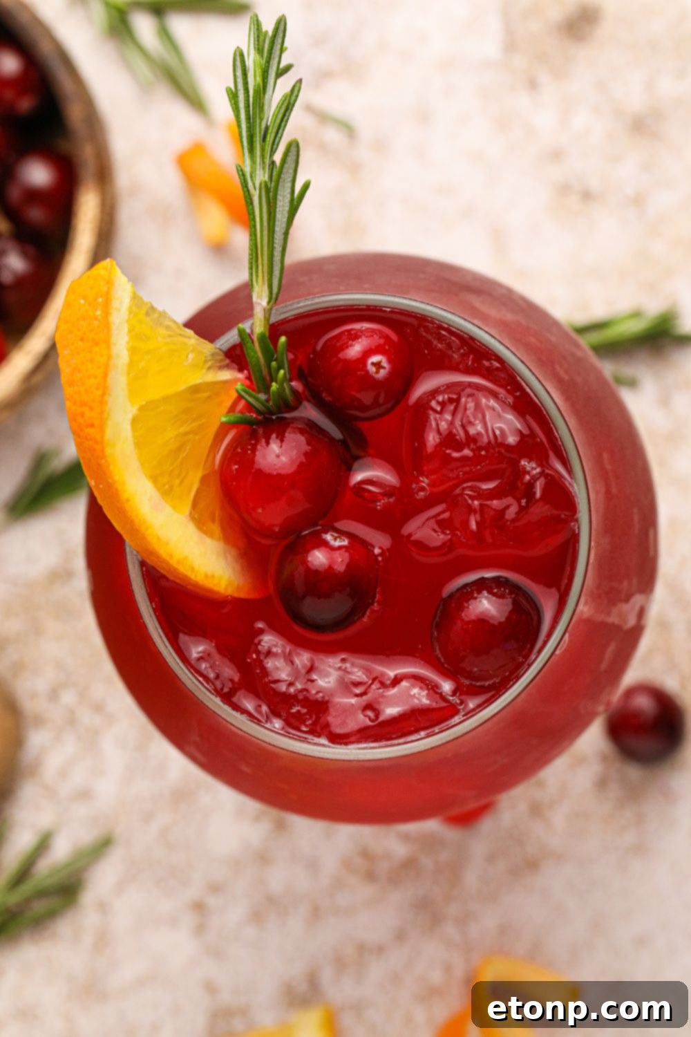 Cranberry Whiskey Sour on table, overhead look into the glass with an orange slice and cranberries in the glass with ice