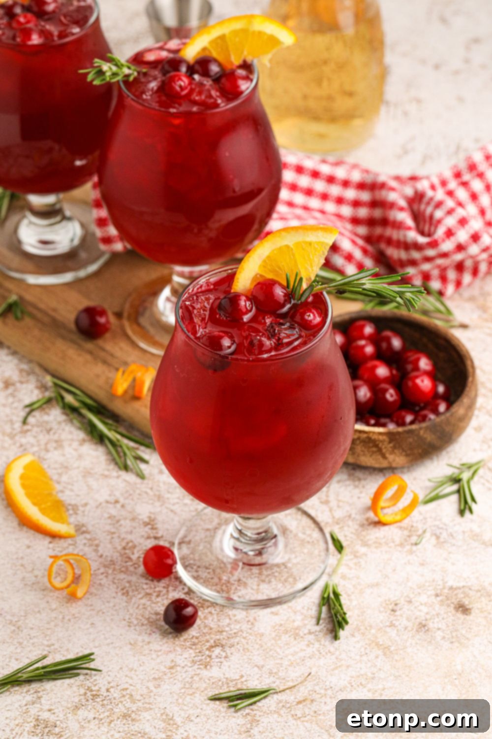 Cocktail glasses filled with Cranberry Whiskey Sour, garnished with orange slices and cranberries scattered on table