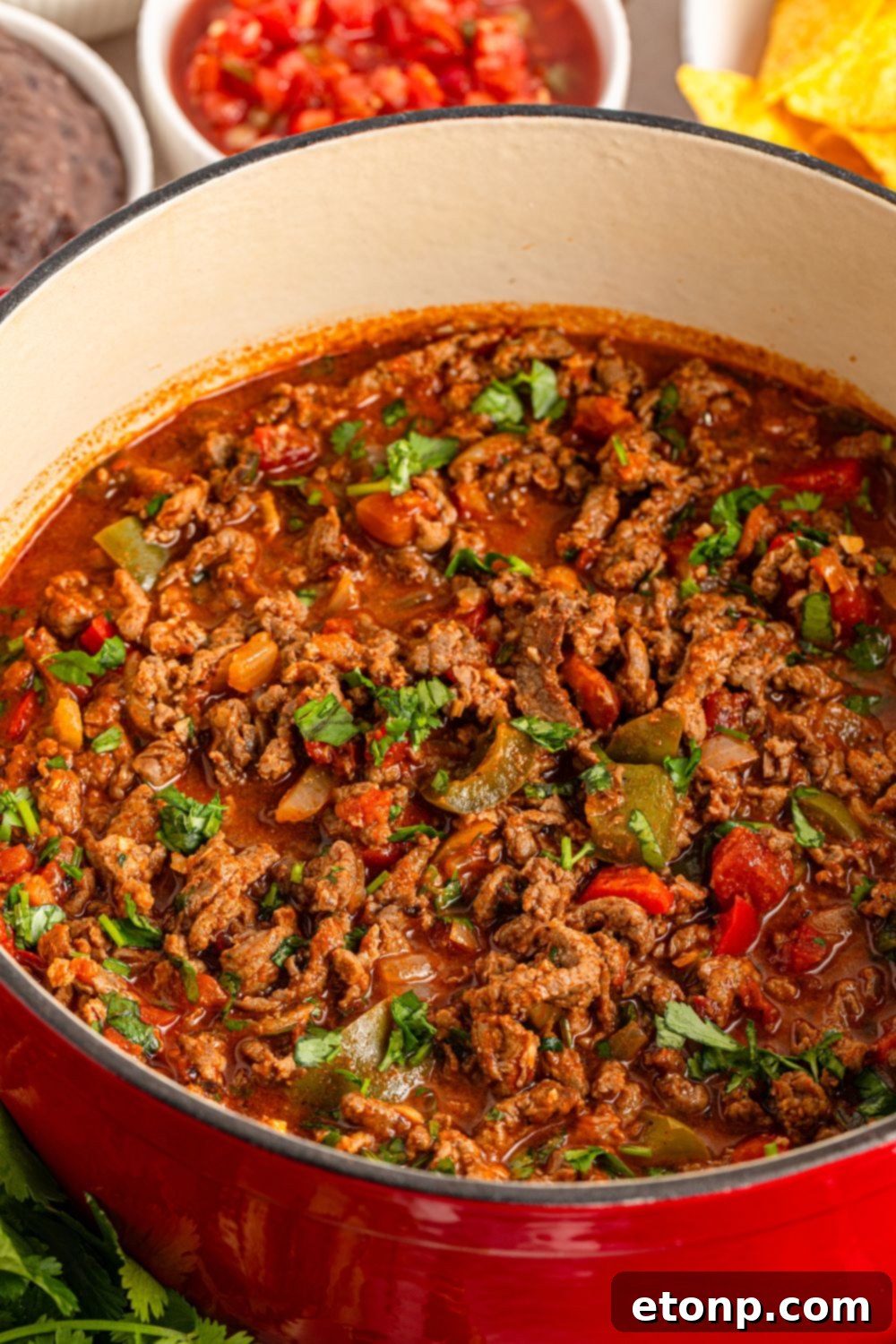 Ground Beef 13 Carne Picada cooked in a Dutch oven with bowls of ingredients around the pan