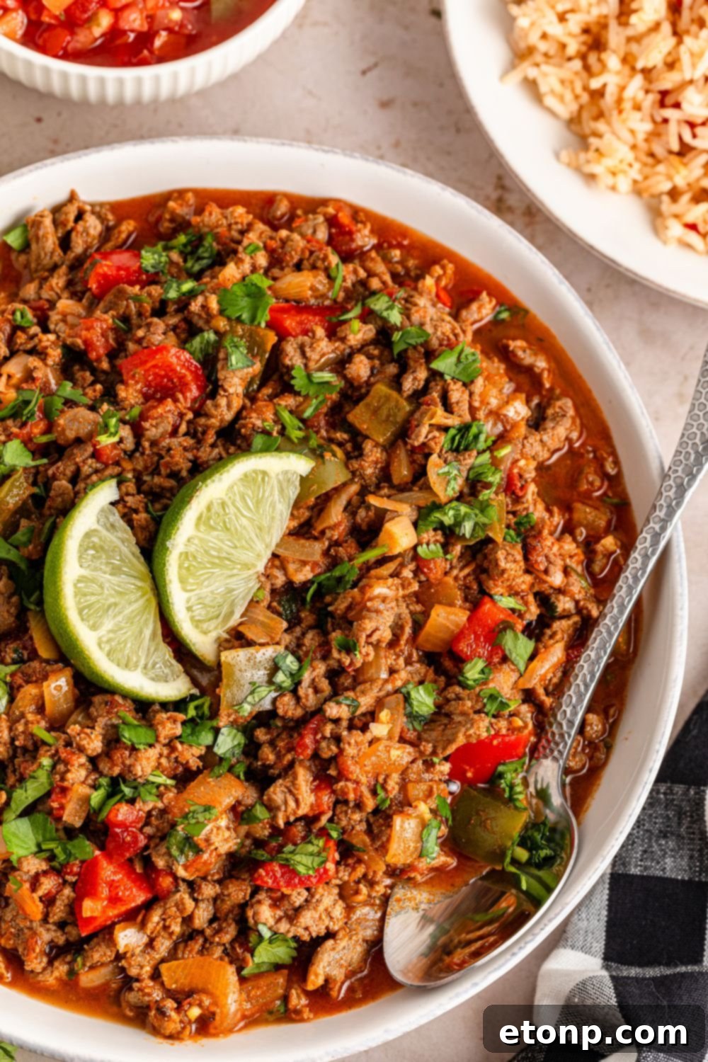 Ground Beef 16 Carne Picada in a bowl with lime wedges in center and a spoon sitting in the bowl