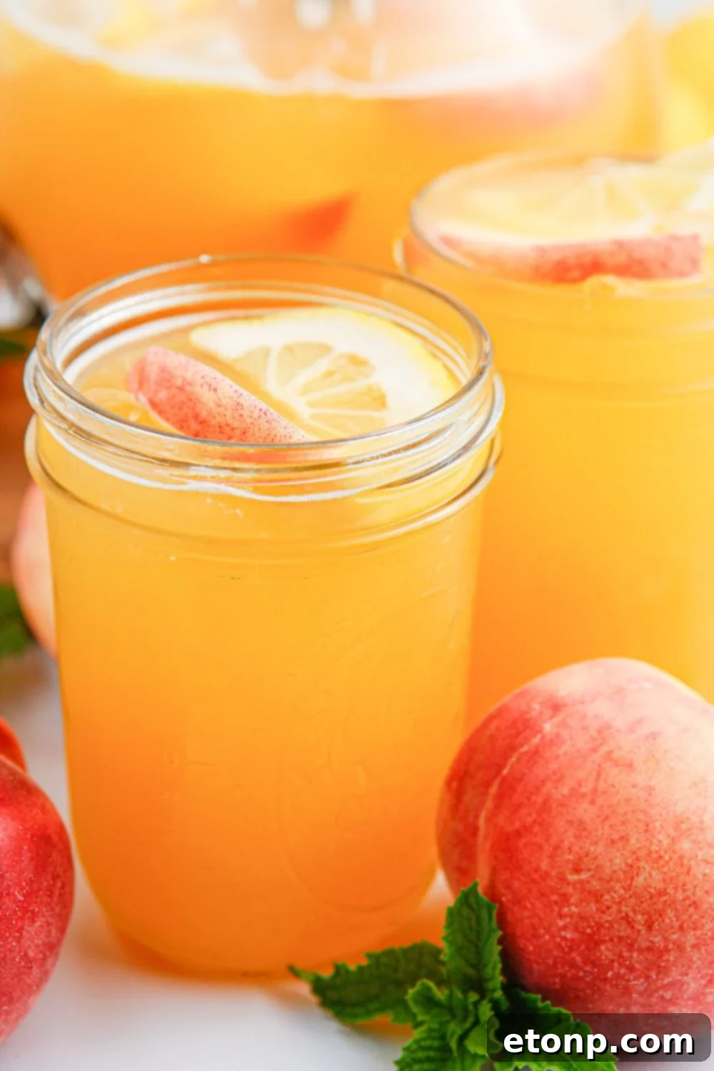 Several mason jars filled with homemade peach lemonade are arranged on a rustic table, with a whole ripe peach placed to the side, emphasizing the wholesome, natural ingredients used in the refreshing drink.
