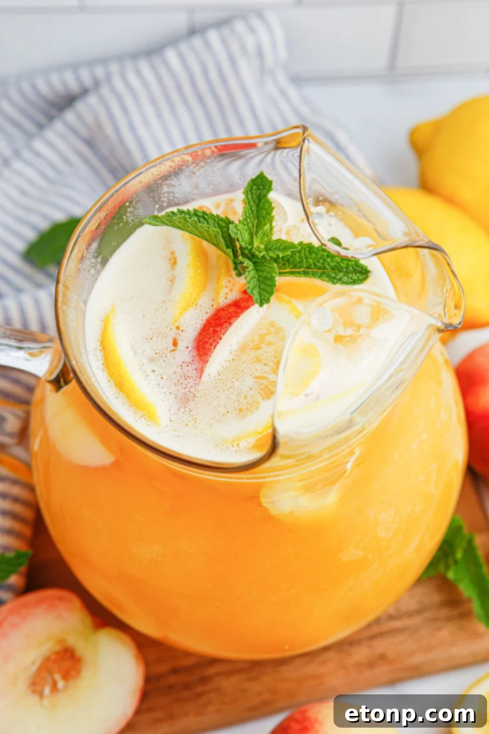 A clear glass pitcher filled with homemade peach lemonade, elegantly garnished with fresh mint sprigs, sits ready to be served, promising a refreshing and flavorful experience for any occasion.