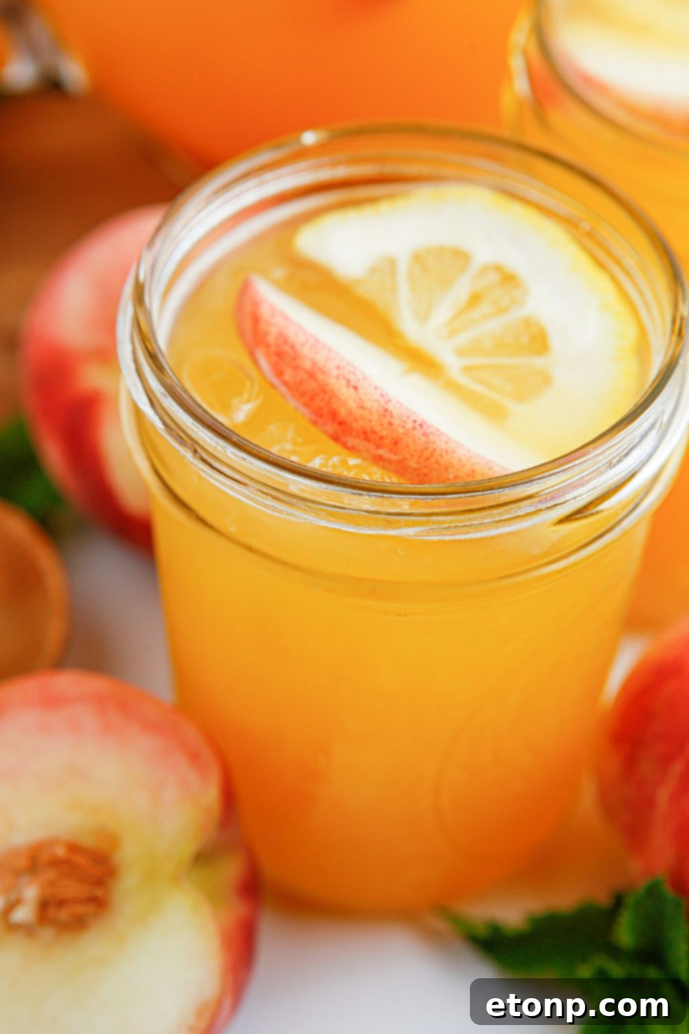 Glasses of peach lemonade, beautifully adorned with fresh fruit slices, are elegantly displayed on a table, offering a vibrant and inviting visual of pure summer refreshment.