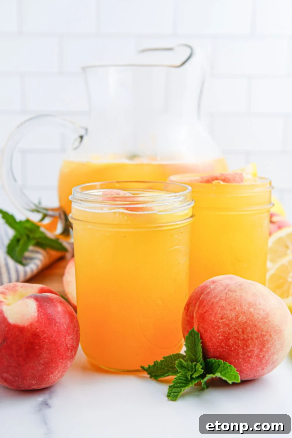Fresh peach lemonade is elegantly displayed on a table in both individual glasses and a clear glass pitcher, creating an inviting and refreshing visual arrangement perfect for any occasion.