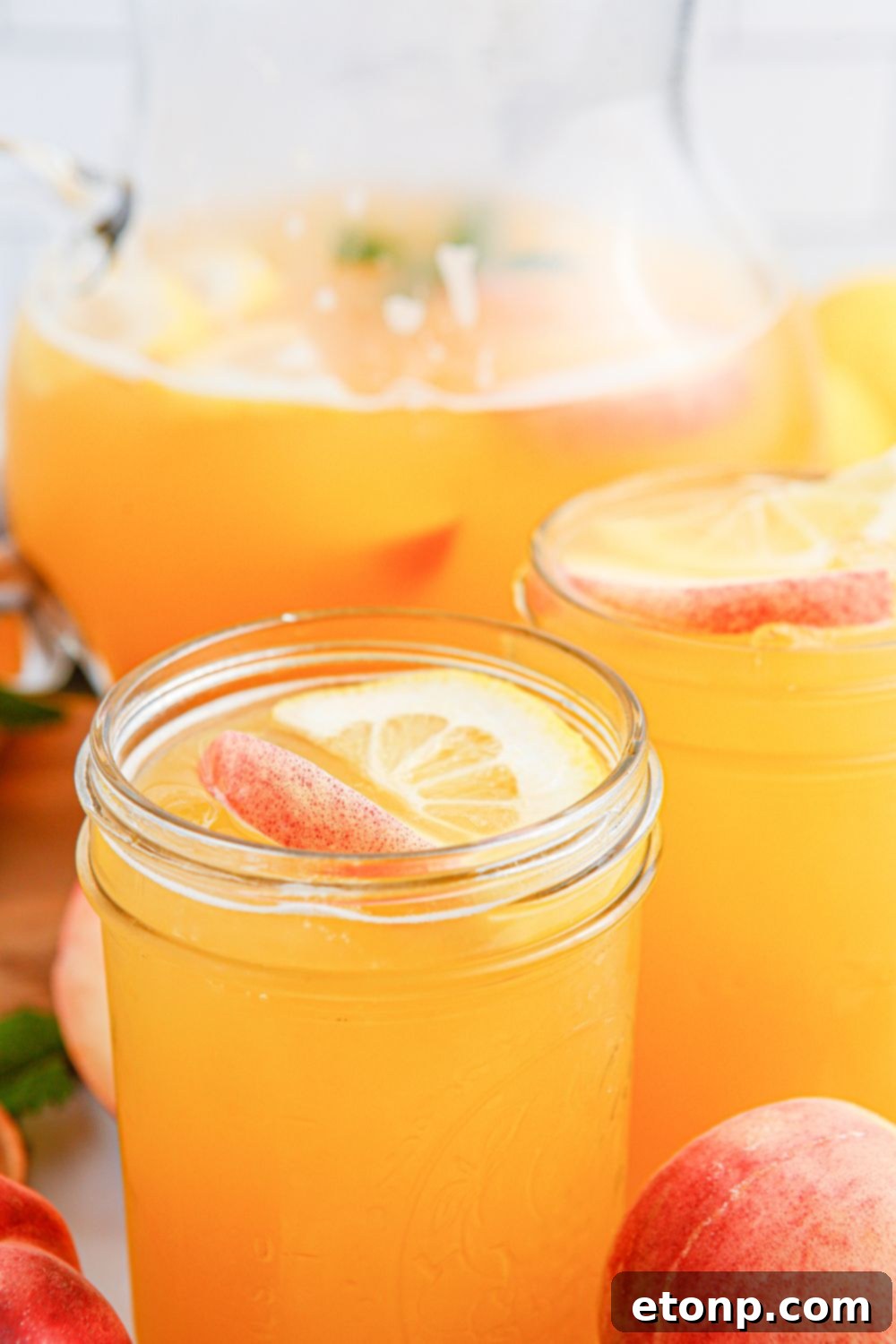 A refreshing glass of peach lemonade, beautifully garnished with vibrant slices of fresh peaches and lemons, perfectly captures the essence of a delightful and cool summer drink.