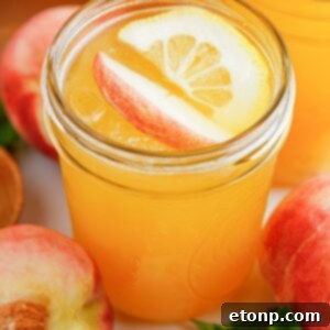 Homemade Peach Lemonade in a mason jar garnished with a peach slice and an orange slice, radiating freshness and the essence of summer flavor.