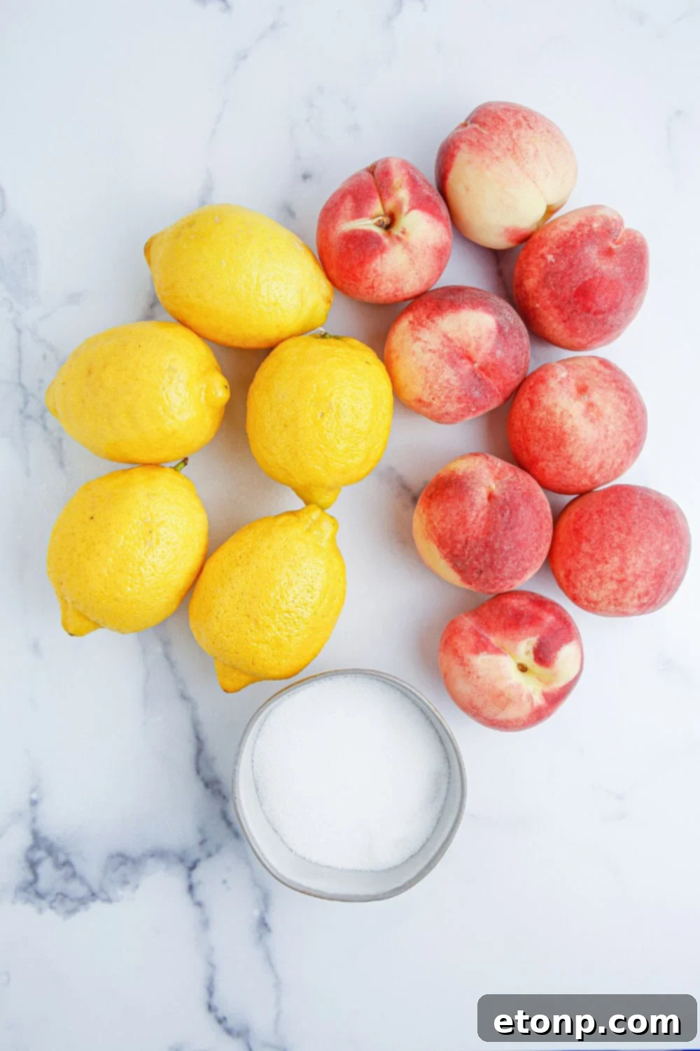 An inviting still life of fresh lemons, ripe peaches, and a bowl of granulated sugar, all resting on a sleek marble countertop, perfectly arranged for the creation of delicious peach lemonade.