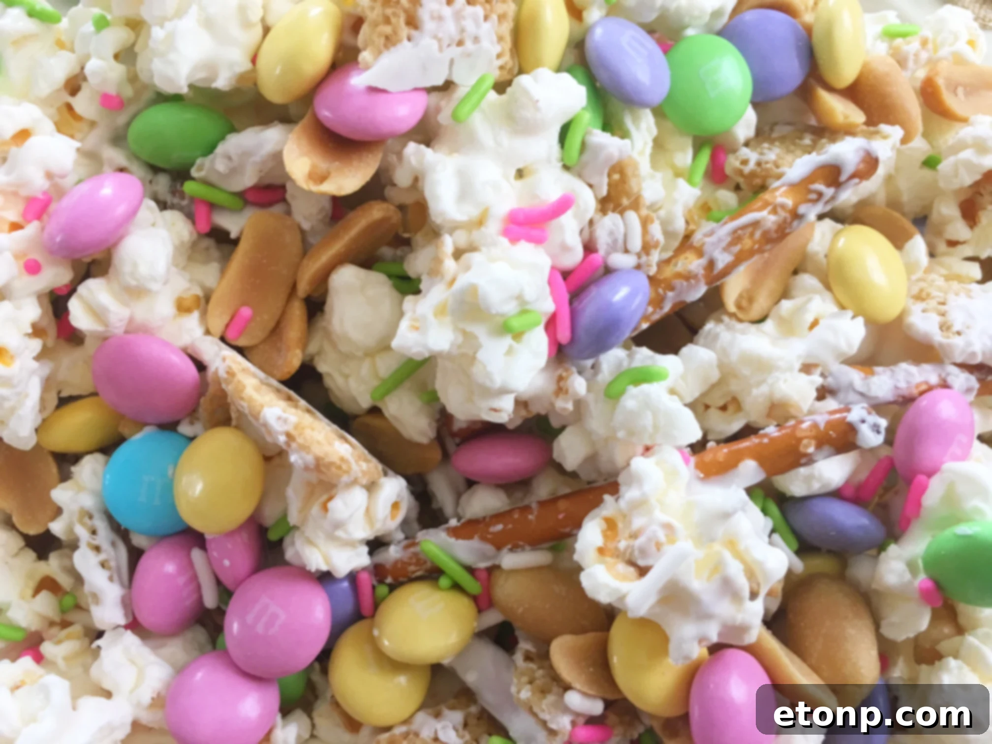 A large bowl of colorful Easter Bunny Bait snack mix with white chocolate coated popcorn, pretzels, Chex cereal, M&Ms, and sprinkles.