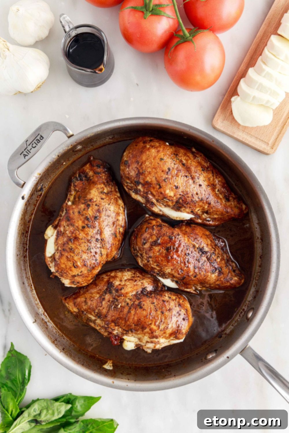 Caprese Stuffed Chicken in a skillet on a table, surrounded by fresh tomatoes, cheese, and basil