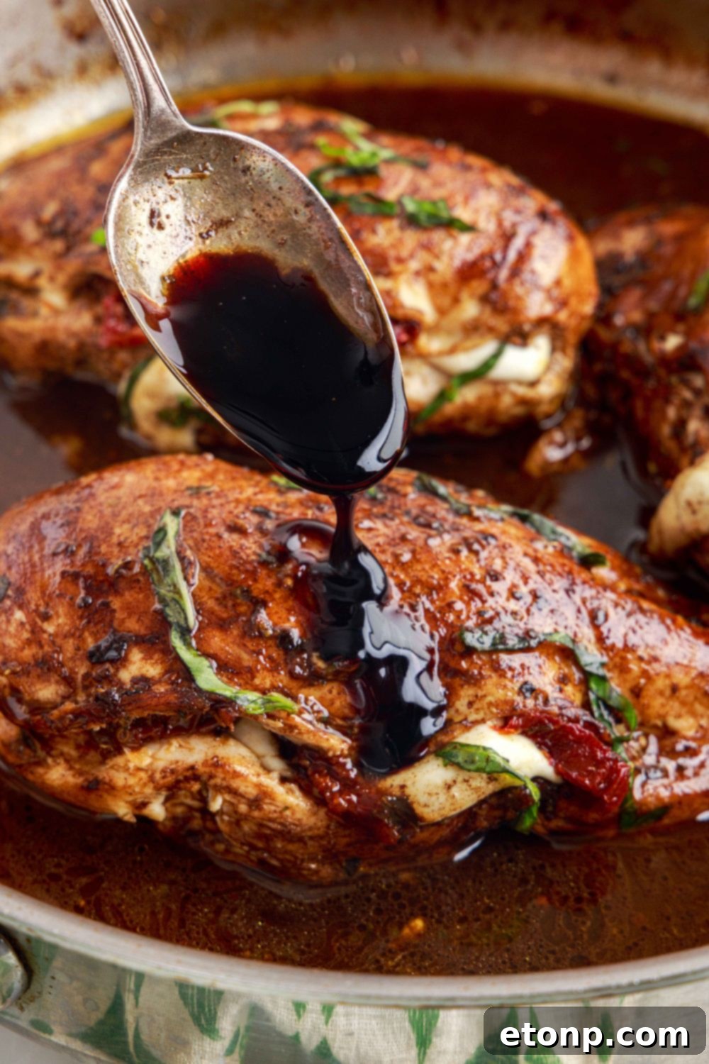 Caprese Stuffed Chicken in a pan with a spoon drizzling balsamic glaze over it