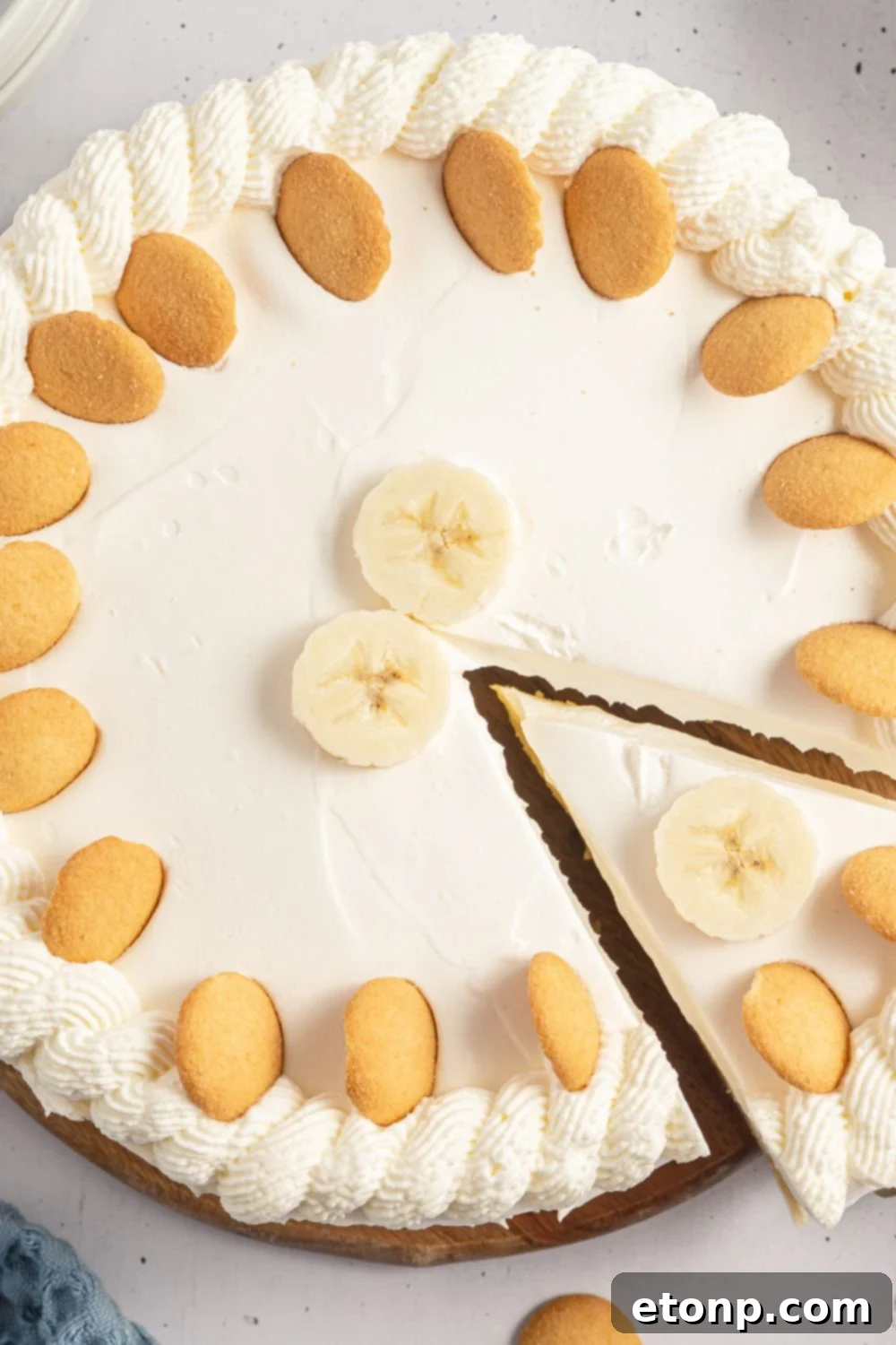 Dreamy No Bake Banana Pudding Cheesecake 14 A whole banana cheesecake on a table with one slice already cut and removed, showcasing the remaining dessert.