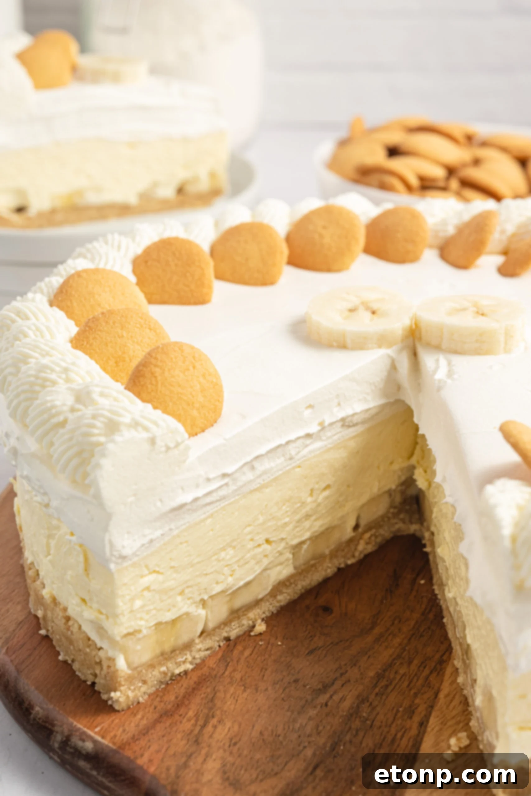 Dreamy No Bake Banana Pudding Cheesecake 17 A banana pudding cheesecake, partially sliced, displayed on a wooden cutting board.