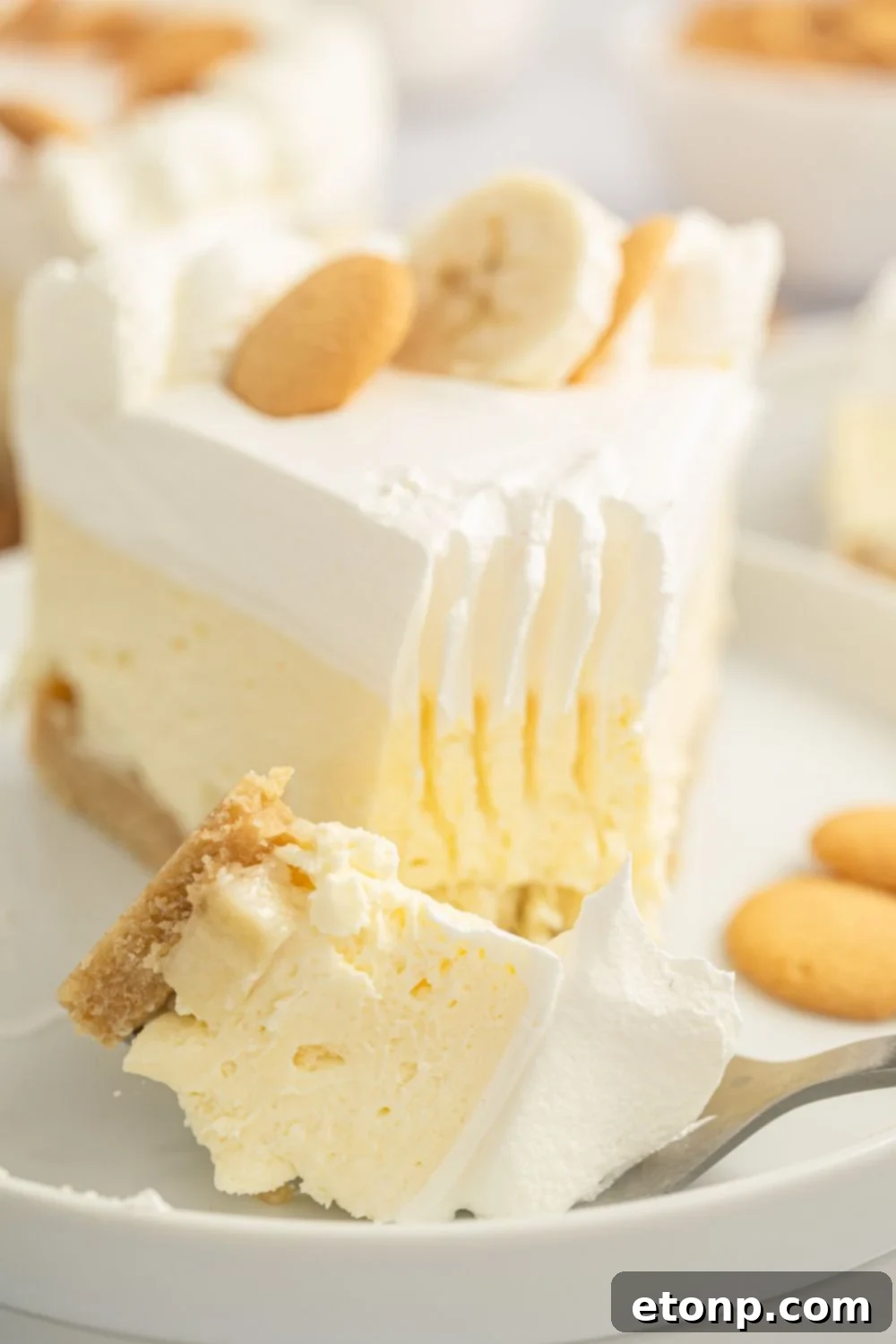 Dreamy No Bake Banana Pudding Cheesecake 19 A slice of No-Bake Banana Pudding Cheesecake on a plate with a fork and a bite taken out.