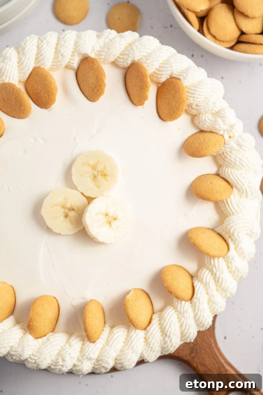 Dreamy No Bake Banana Pudding Cheesecake 4 Whole No-Bake Banana Pudding Cheesecake sitting on a wooden cutting board on a table.