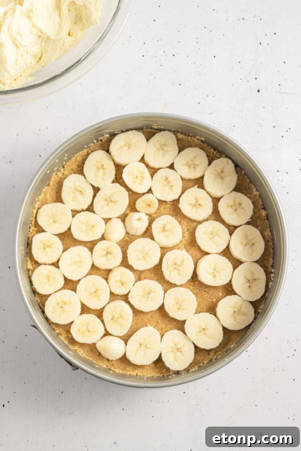Dreamy No Bake Banana Pudding Cheesecake 8 Vanilla wafer crust neatly pressed into a springform pan, with a layer of sliced bananas on top.