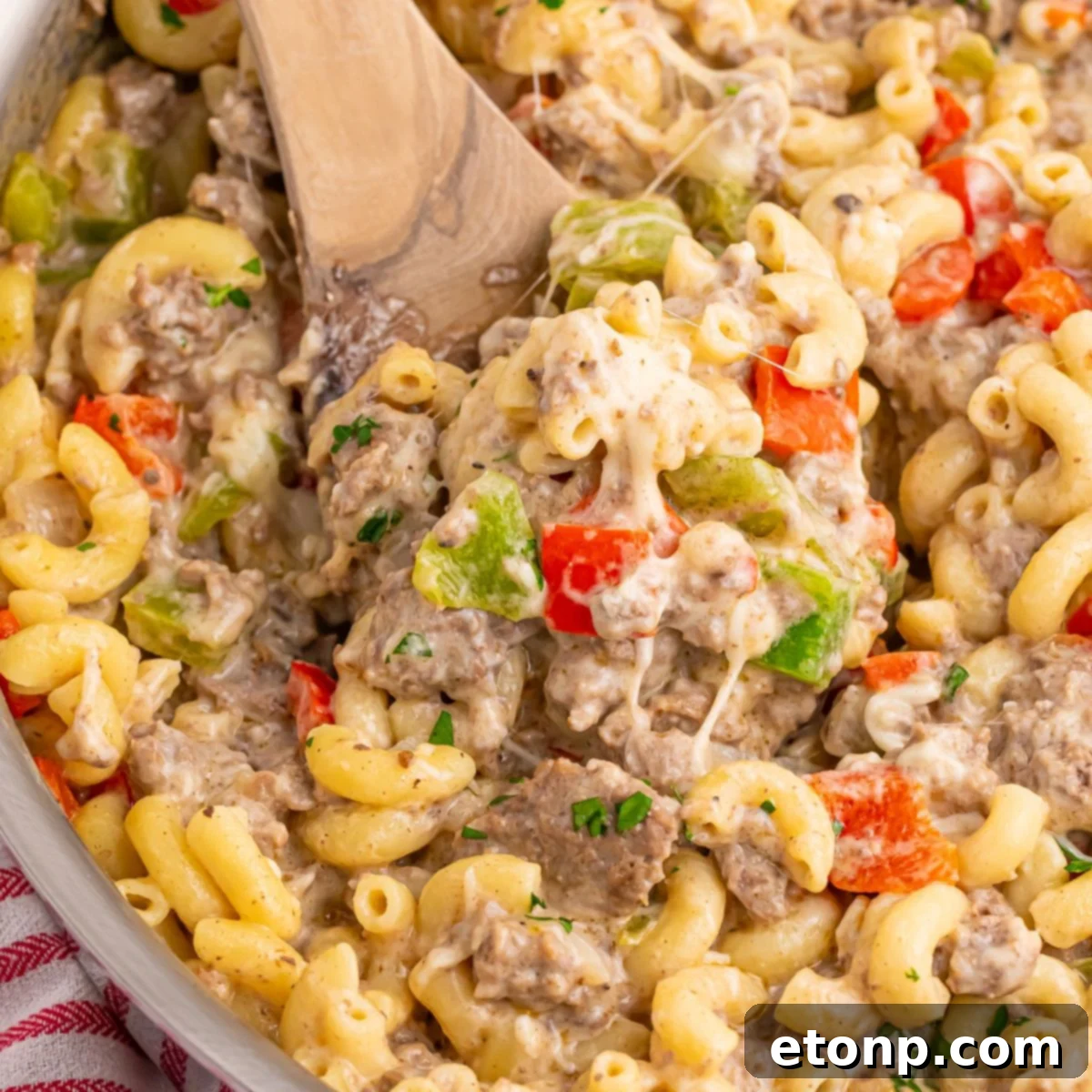 Philly Cheesesteak Pasta in a pan with a wooden spatula with some of the mixture on it 