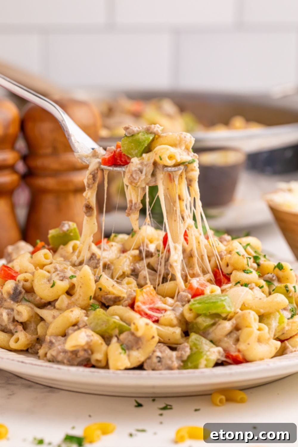 Philly Cheesesteak Pasta on a plate with a fork full pulling up showing the strings of cheese 