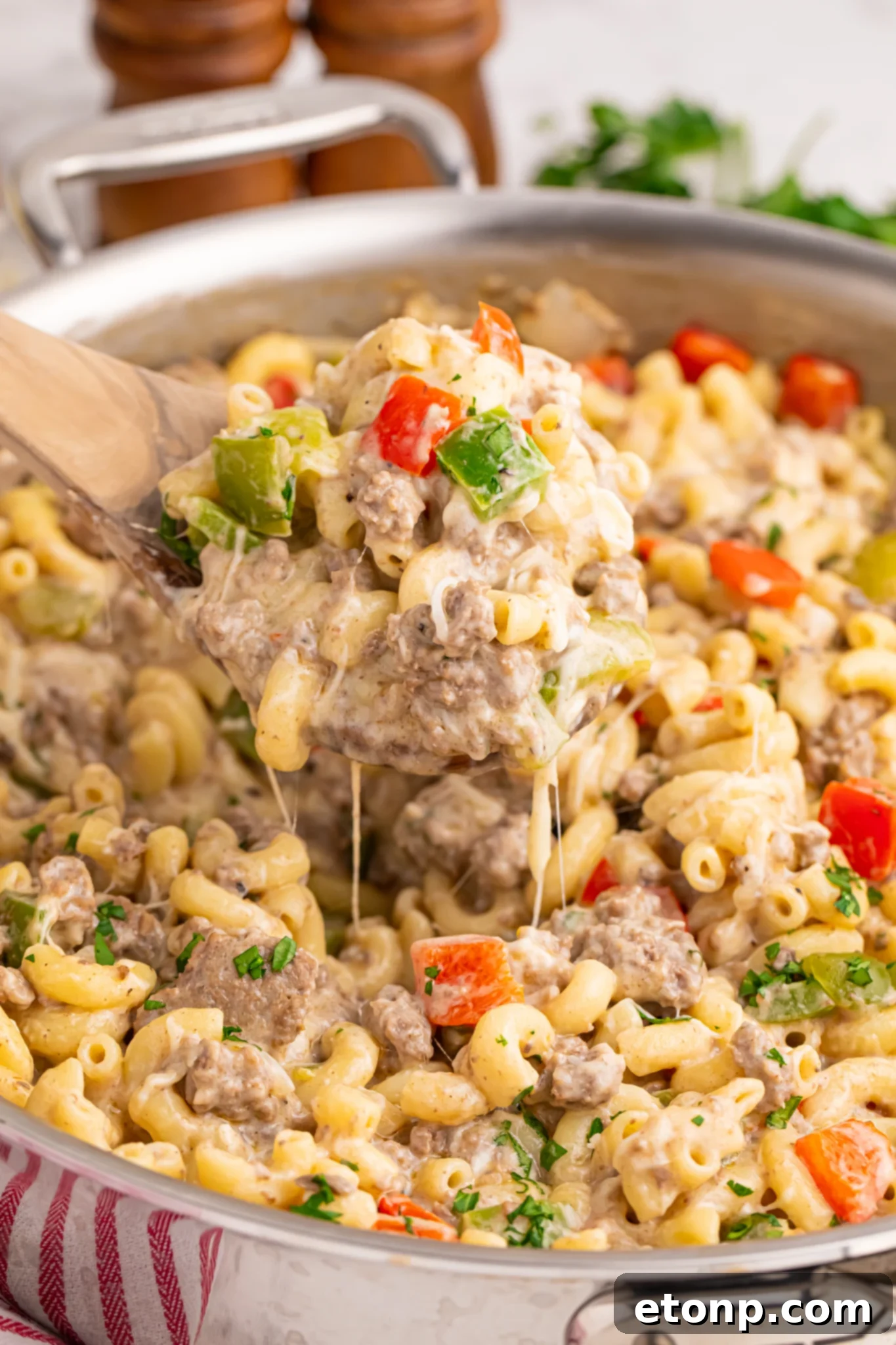 Philly Cheesesteak Pasta in a skillet on table with spoon lifting up a large bite