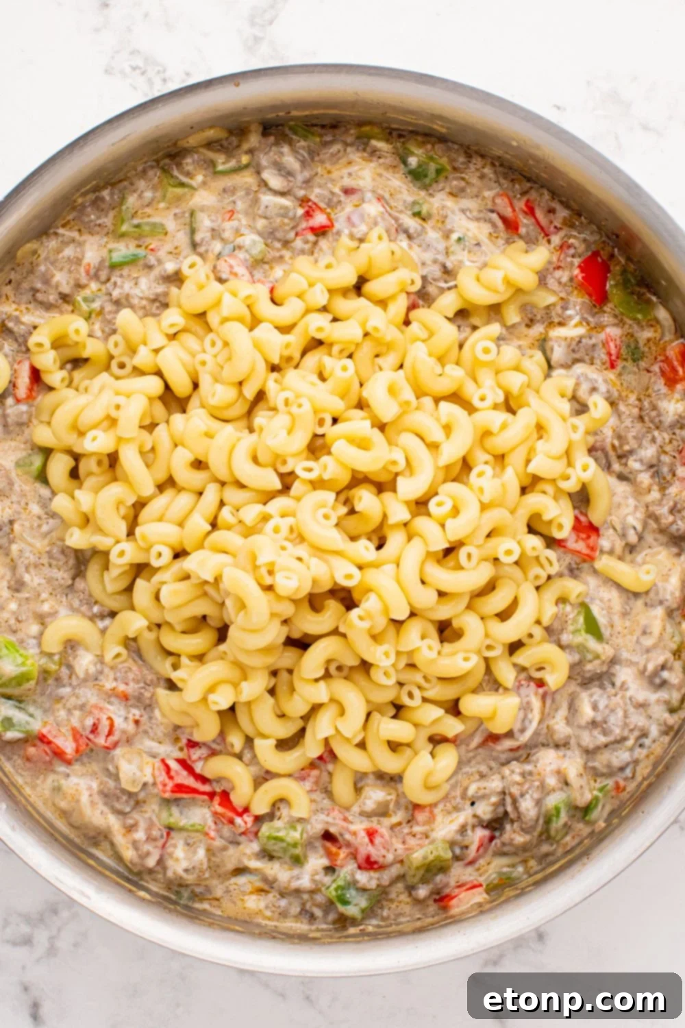 Philly Cheesesteak Pasta mixture in a pan with cooked pasta poured on top of the meat mixture 