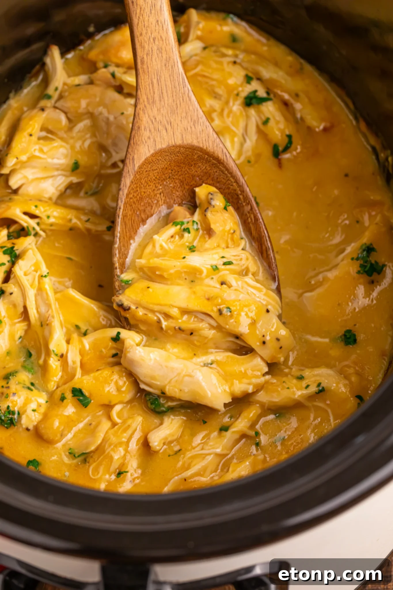 overhead look of crockpot with chicken and gravy in it with a wooden spoon with some meat and gravy on it 