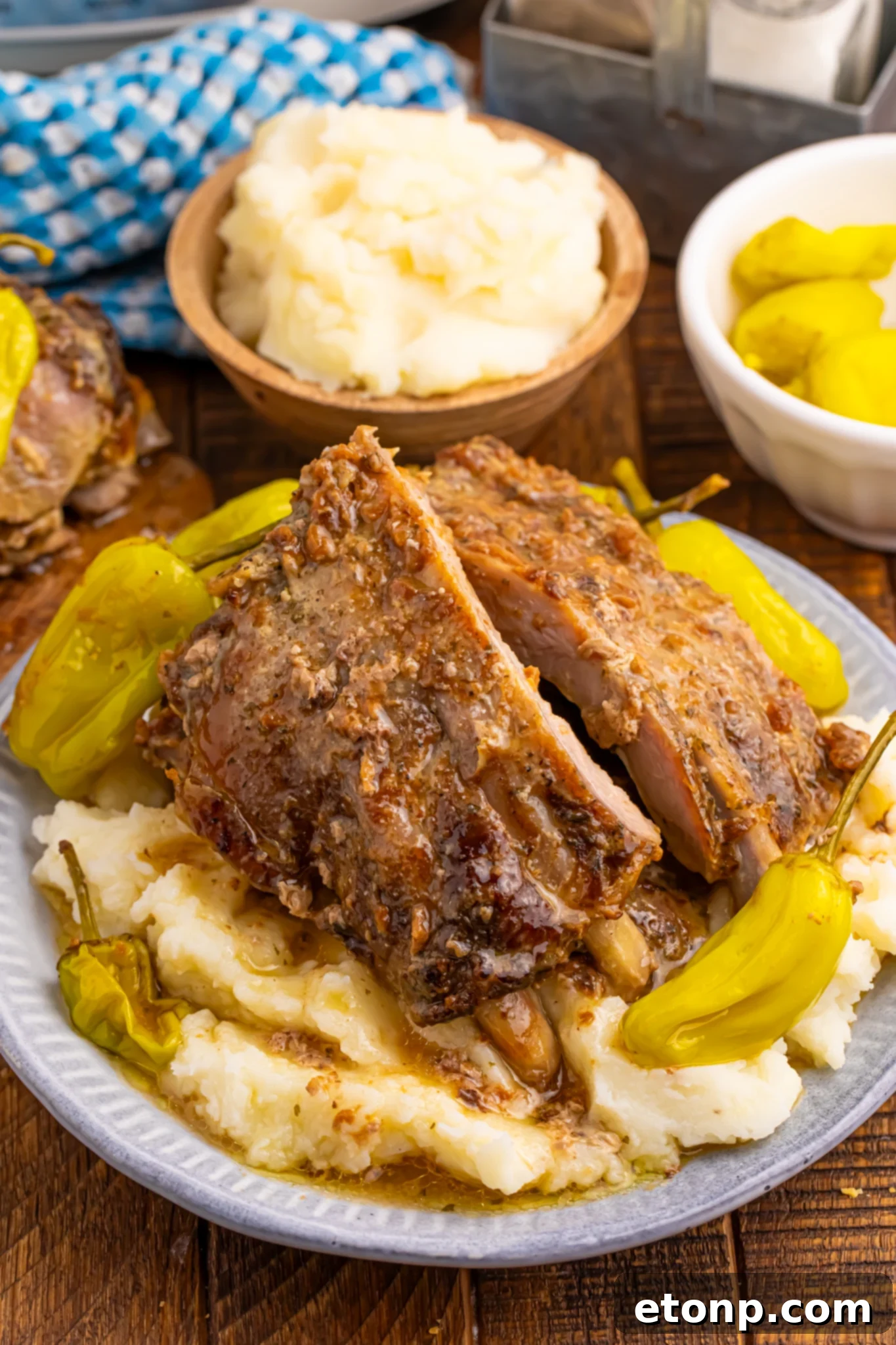 Slow Cooker Mississippi Ribs on a white plate sitting on top of creamy mashed potatoes, garnished with fresh herbs and a drizzle of sauce.