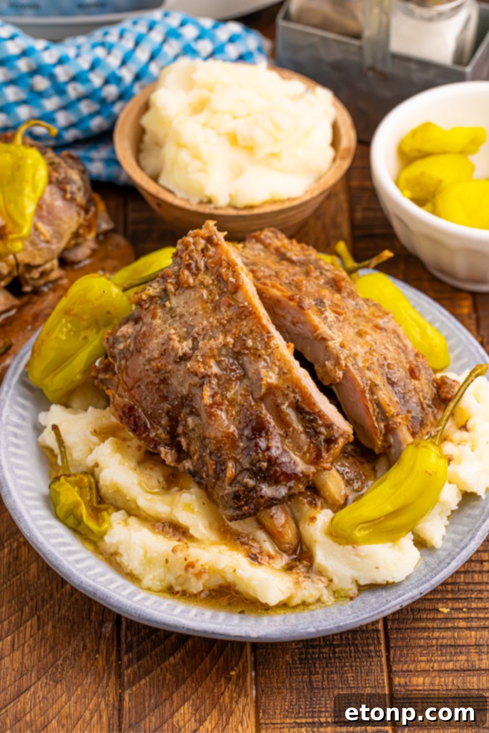 A perfectly plated dinner of Slow Cooker Mississippi Ribs, mashed potatoes, and pepperoncini peppers, drizzled with rich sauce.