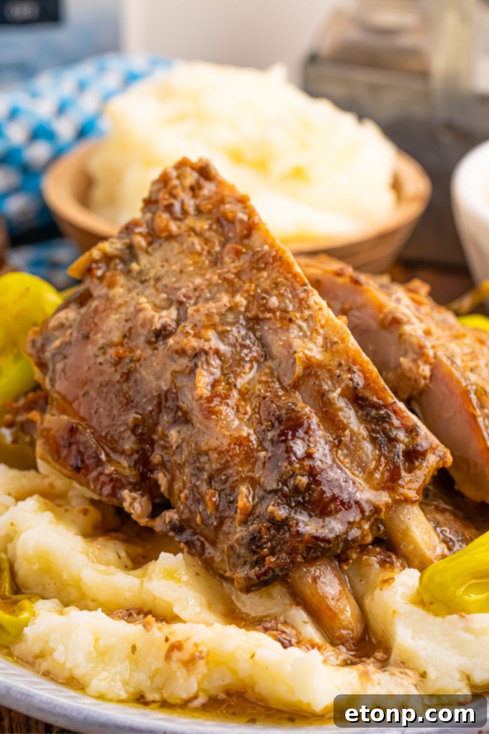 Mississippi Ribs served on a bed of mashed potatoes with vibrant pepperoncini peppers on a white plate, ready to be enjoyed.