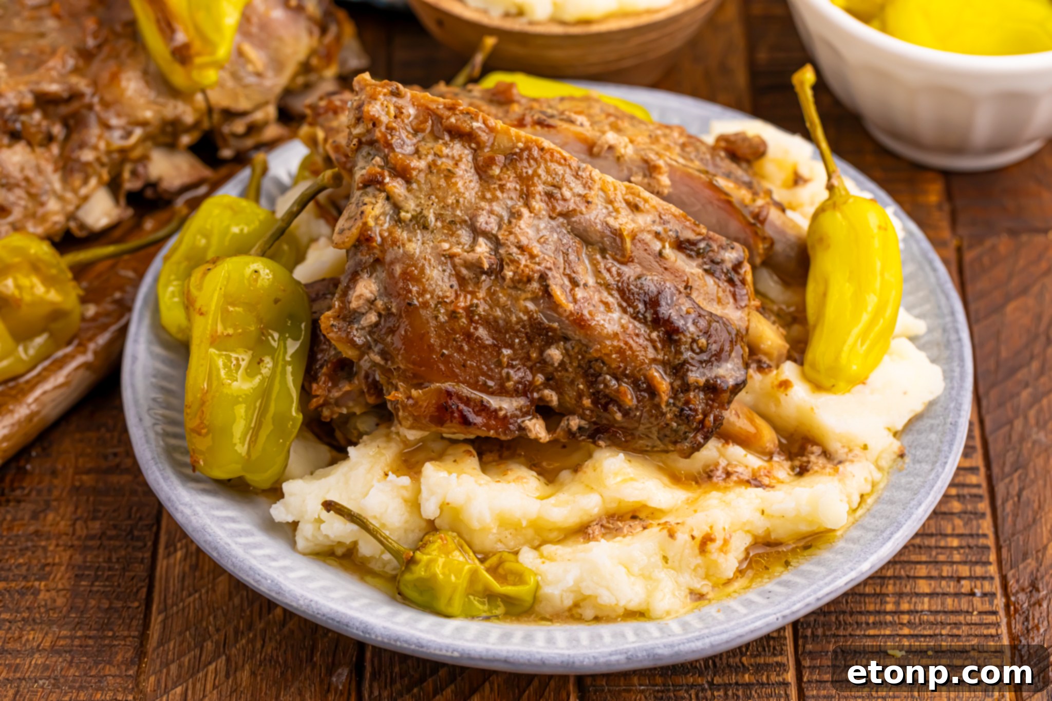 Slow Cooker Mississippi Ribs elegantly plated on a white dish, generously smothered in their savory gravy and served atop a bed of fluffy mashed potatoes.