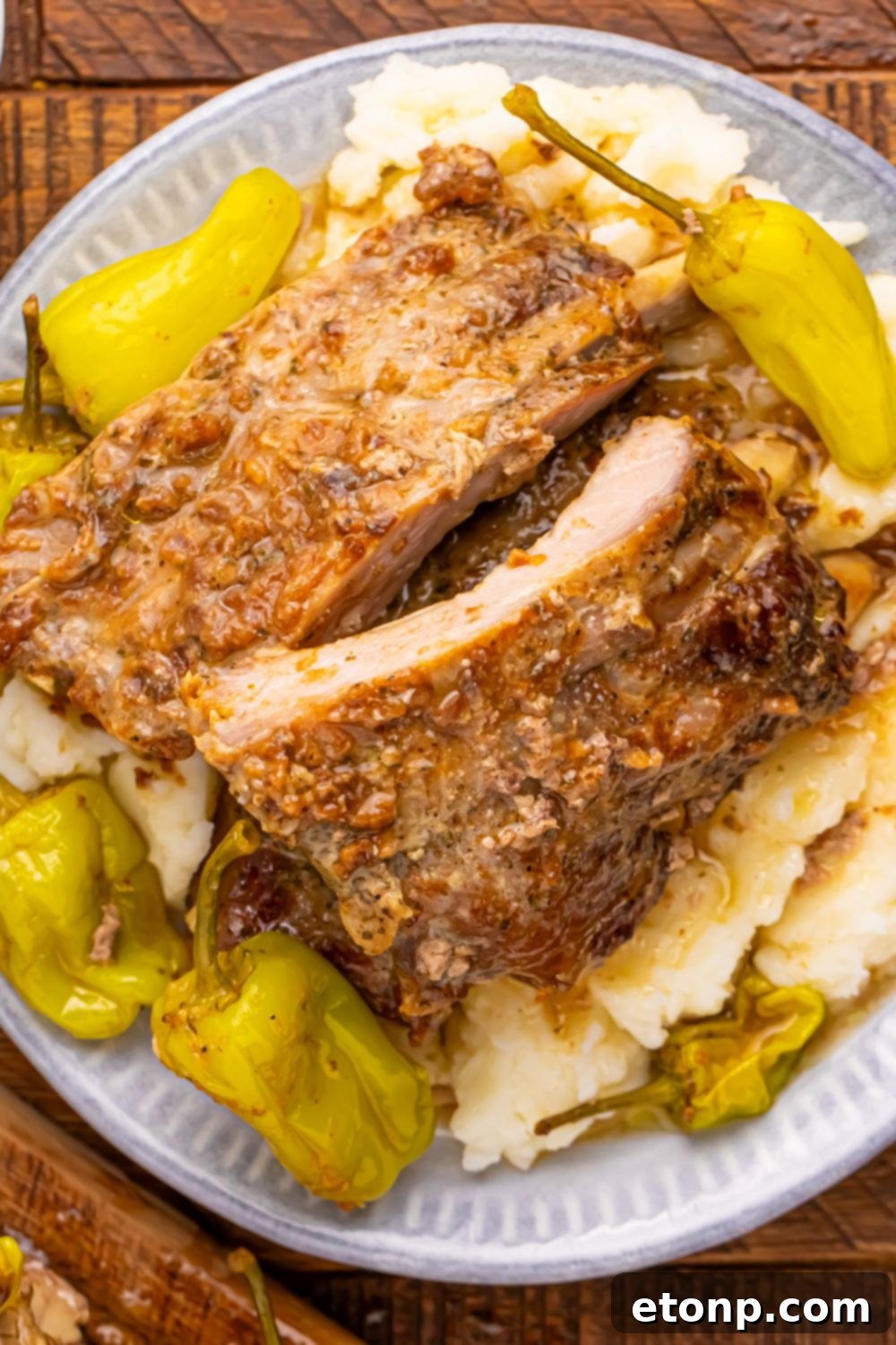 A rustic presentation of a plate filled with baby back ribs, mashed potatoes, and pepperoncini peppers, placed on a wooden table.