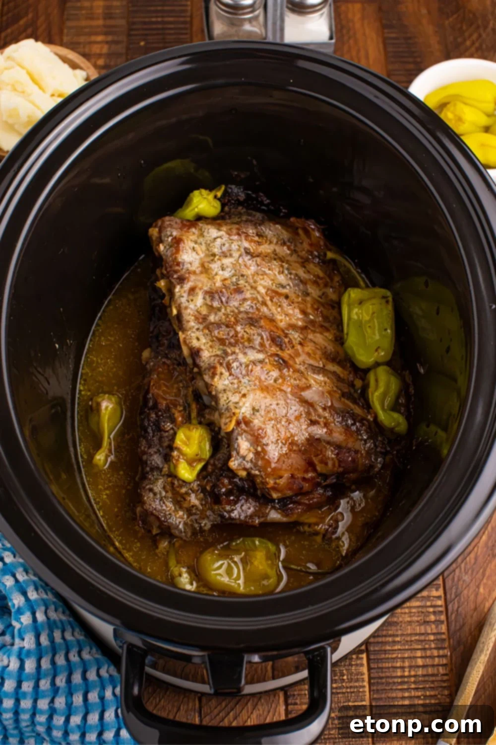 Succulent baby back pork ribs, perfectly cooked and glistening with sauce, resting within a slow cooker on a wooden table, ready for serving.