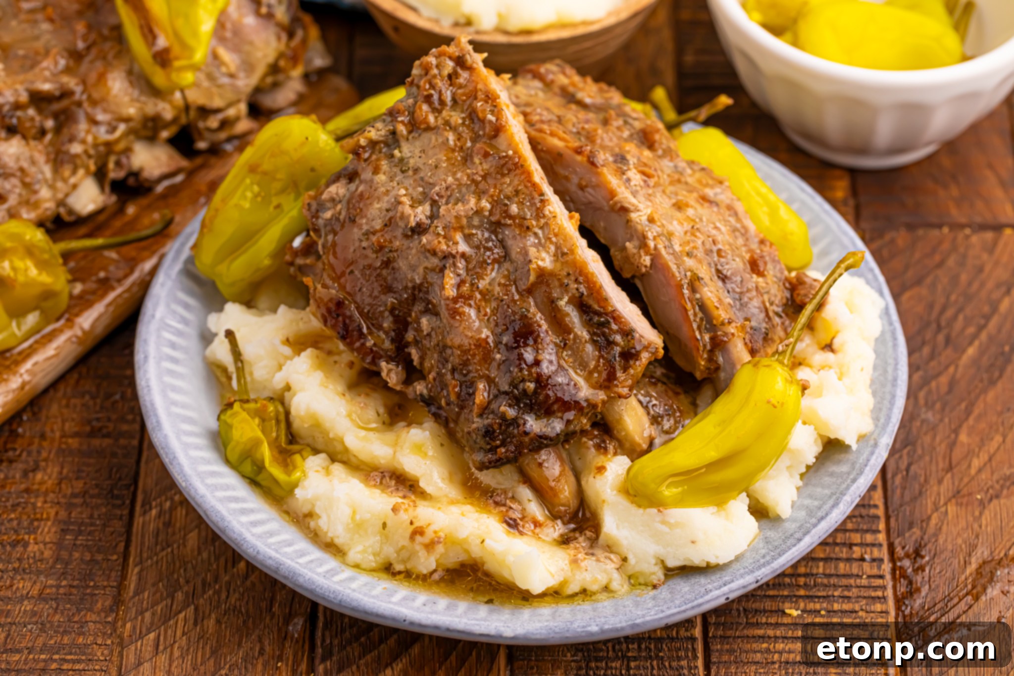 A pristine white plate showcasing Slow Cooker Mississippi Ribs, beautifully arranged over a bed of mashed potatoes, garnished with fresh peppers.