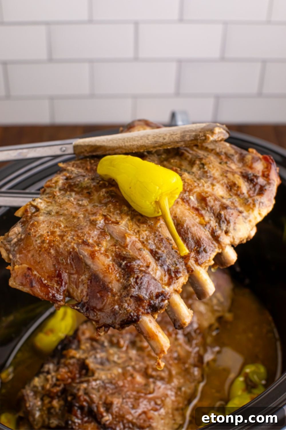 Tender baby back ribs being carefully held with tongs above the slow cooker, ready to be transferred to a cutting board for serving.