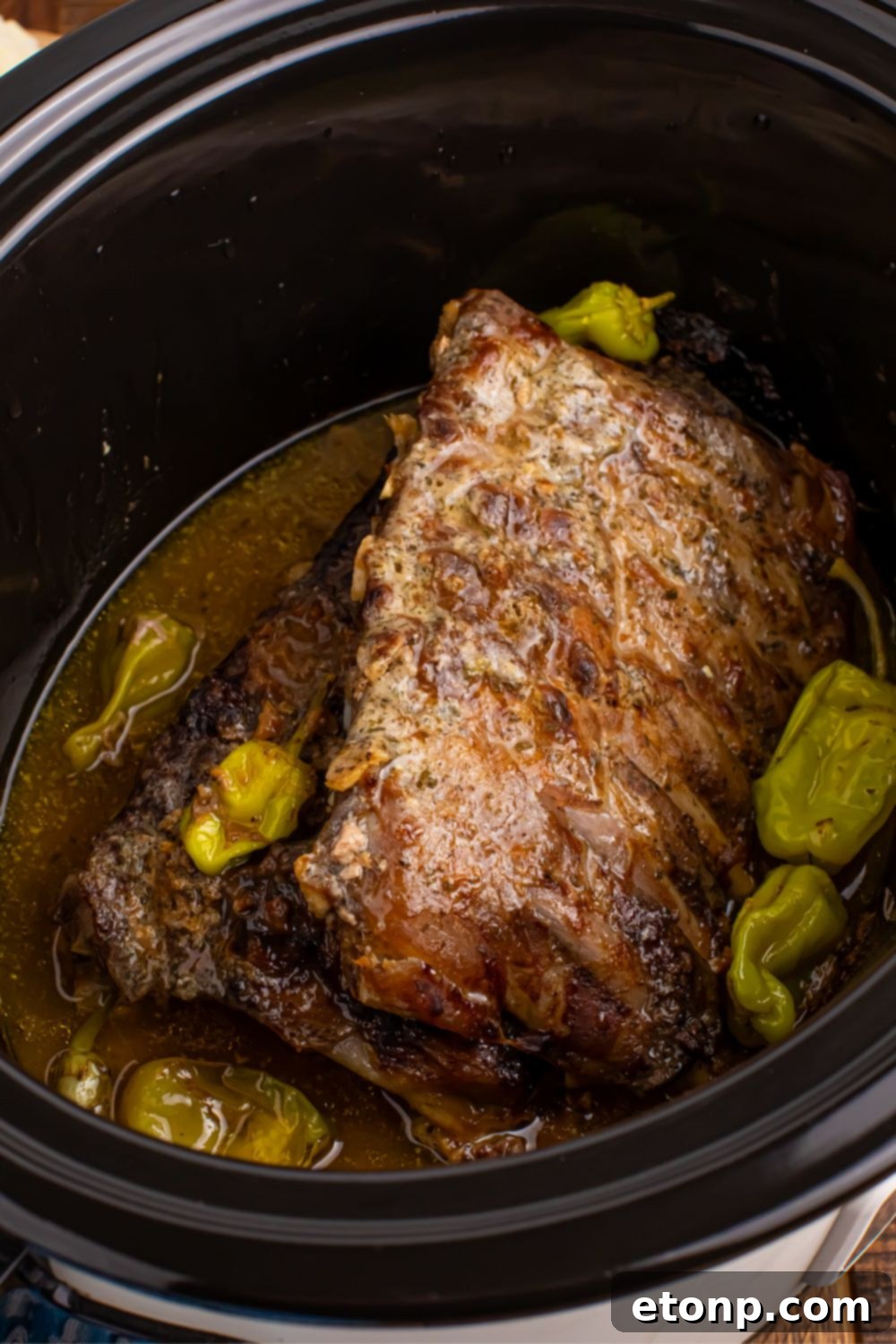 Slow Cooker Mississippi Ribs nestled in a slow cooker, surrounded by vibrant pepperoncini peppers and rich, simmering juices.
