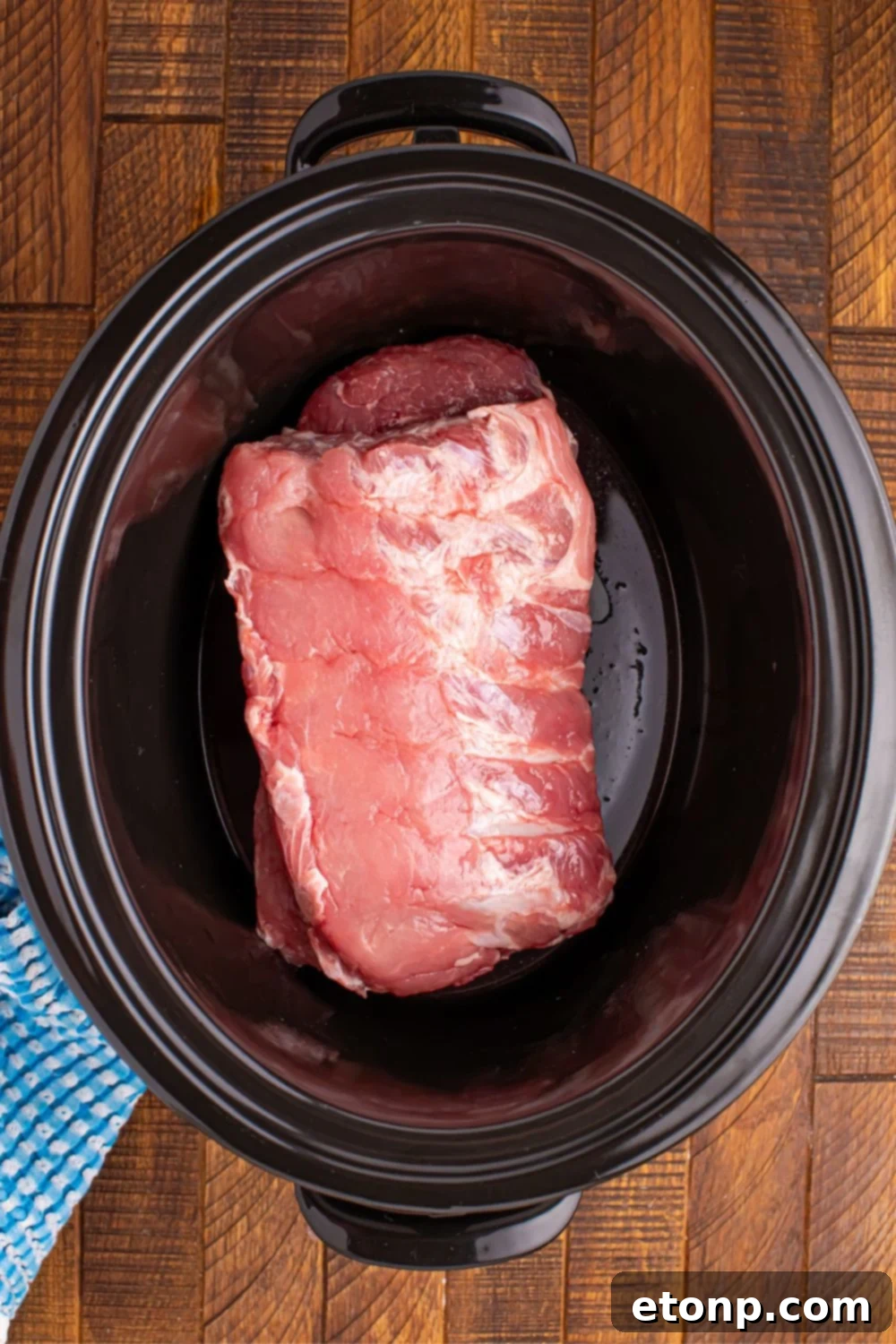 Raw baby back pork ribs neatly arranged in the bottom of a slow cooker, ready for seasoning.