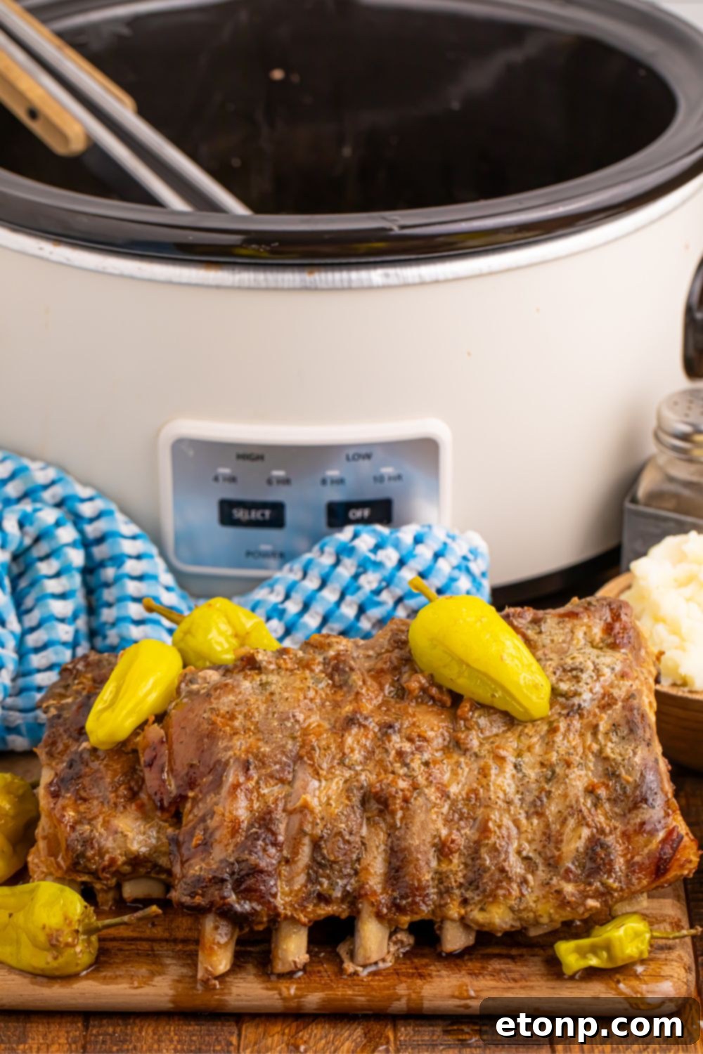 Cooked Mississippi Ribs neatly arranged on a wooden cutting board, with the slow cooker blurred in the background, ready for carving.