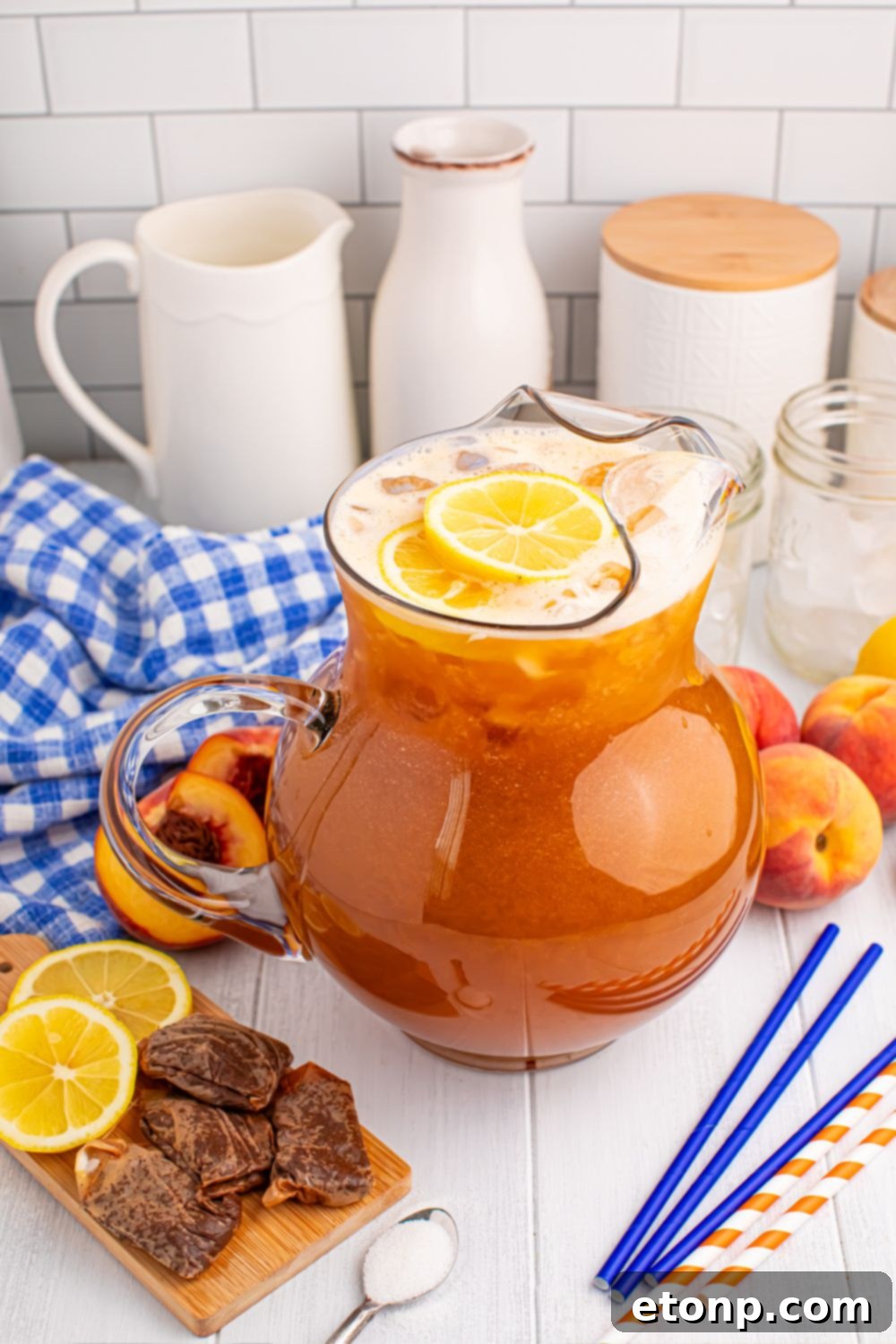 Southern Peach Infusion 12 large pitcher of peach sweet tea on table with straws, sugar, lemon slices and more around the pitcher