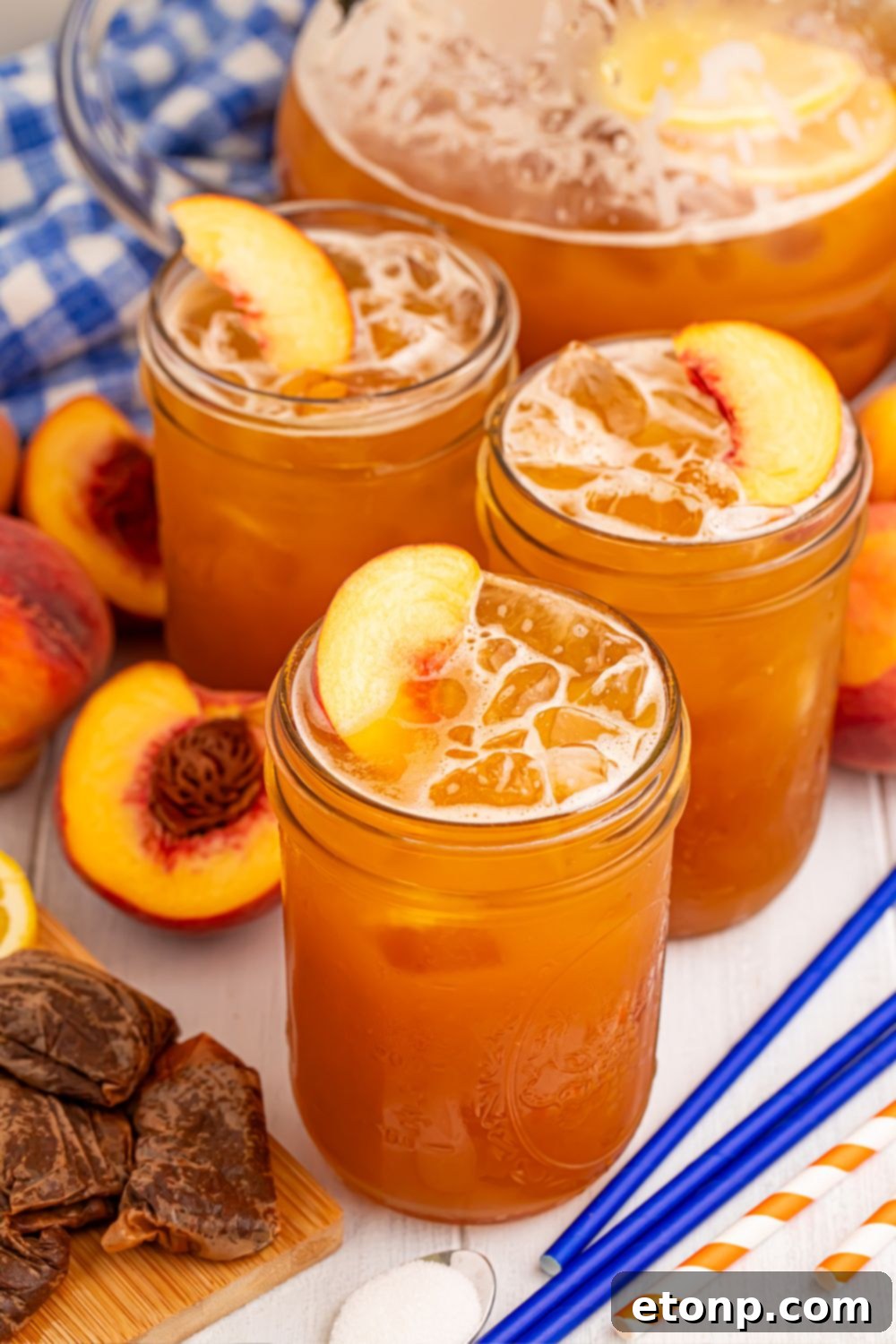 Southern Peach Infusion 14 Peach Sweet Tea in a pitcher on table with 3 glasses in front of it, with tea bags, sliced peaches and more around it