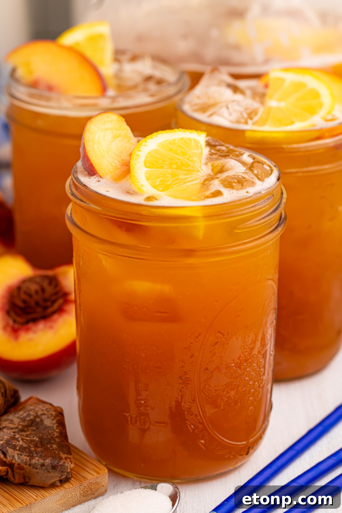 Southern Peach Infusion 15 side view of glass full of peach sweet tea with fruit around the glass on table