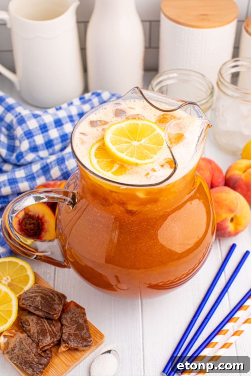 Southern Peach Infusion 19 peach tea on the table with wet tea bags, slices of fruit, straws, sugar, and a blue checked towel around the container