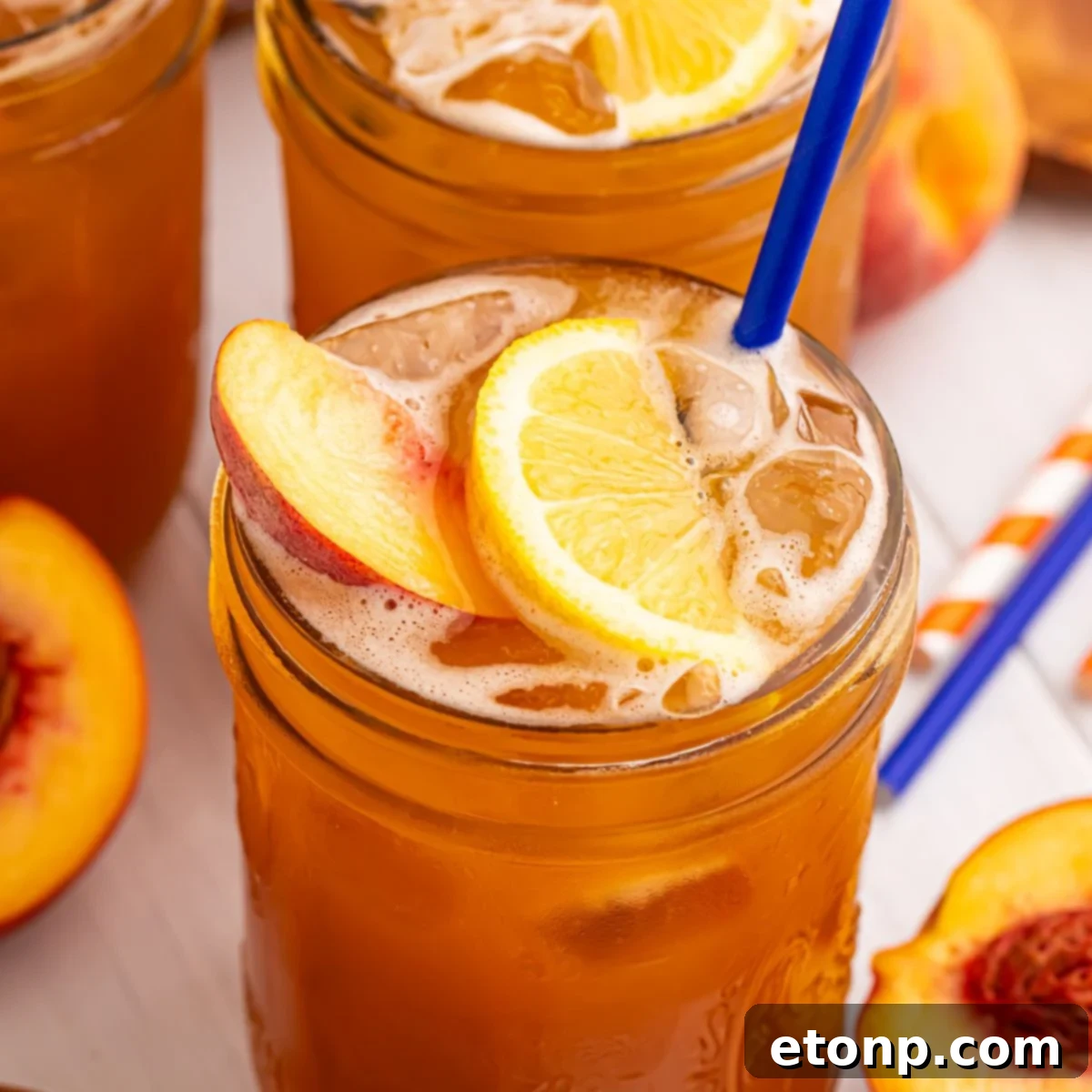 Southern Peach Infusion 3 Peach Sweet Tea in mason jars sitting on table and garnished with a lemon wedge, peach slice, and a blue straw