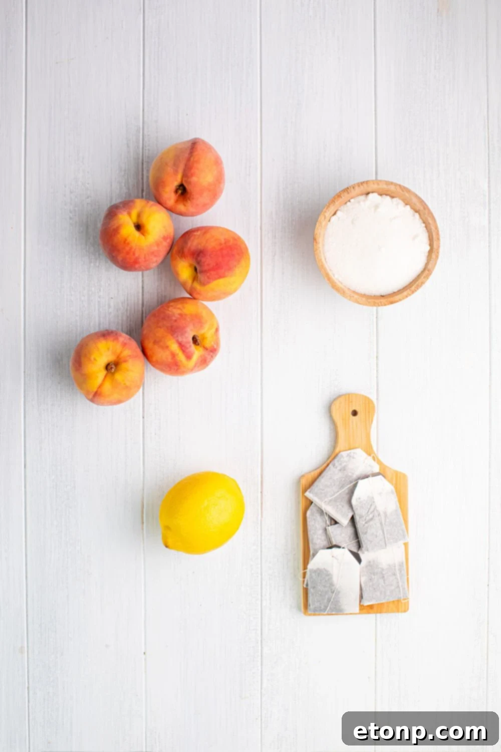 Southern Peach Infusion 6 peaches, lemon, a bowl of sugar, and tea bags are sitting on a table to show ingredients for this peach sweet tea