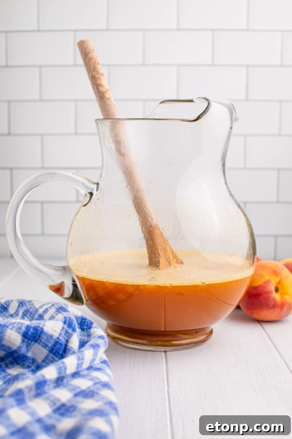 Southern Peach Infusion 10 peach blended mixture in a large pitcher being stirred with a wooden spoon