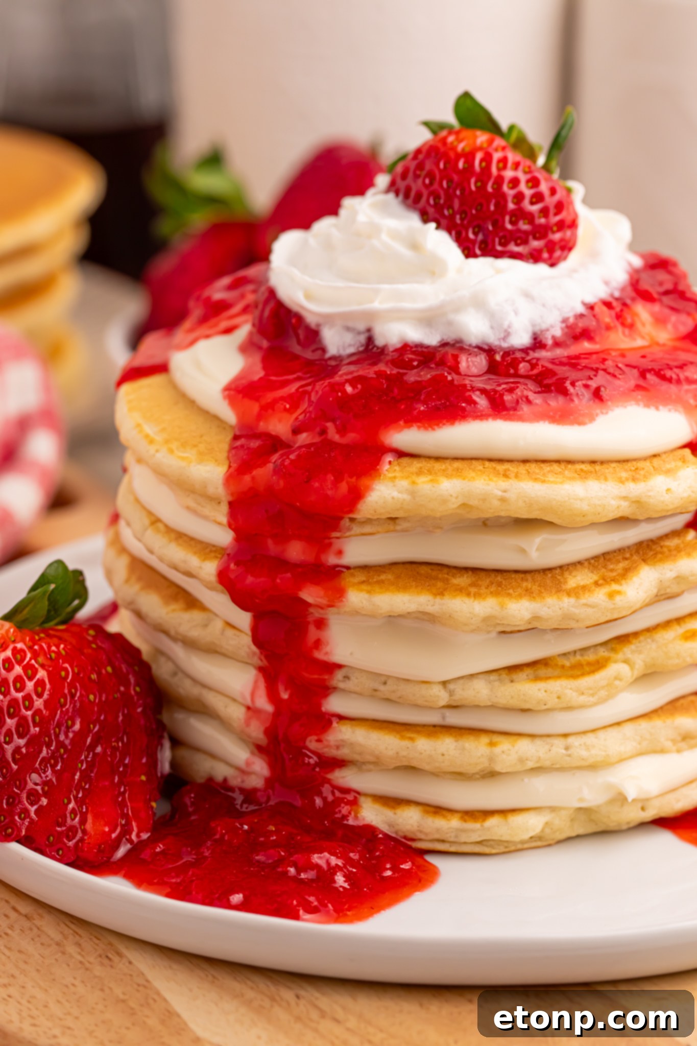 Stacked Strawberry Cheesecake Pancakes drizzled with strawberry sauce on a white plate