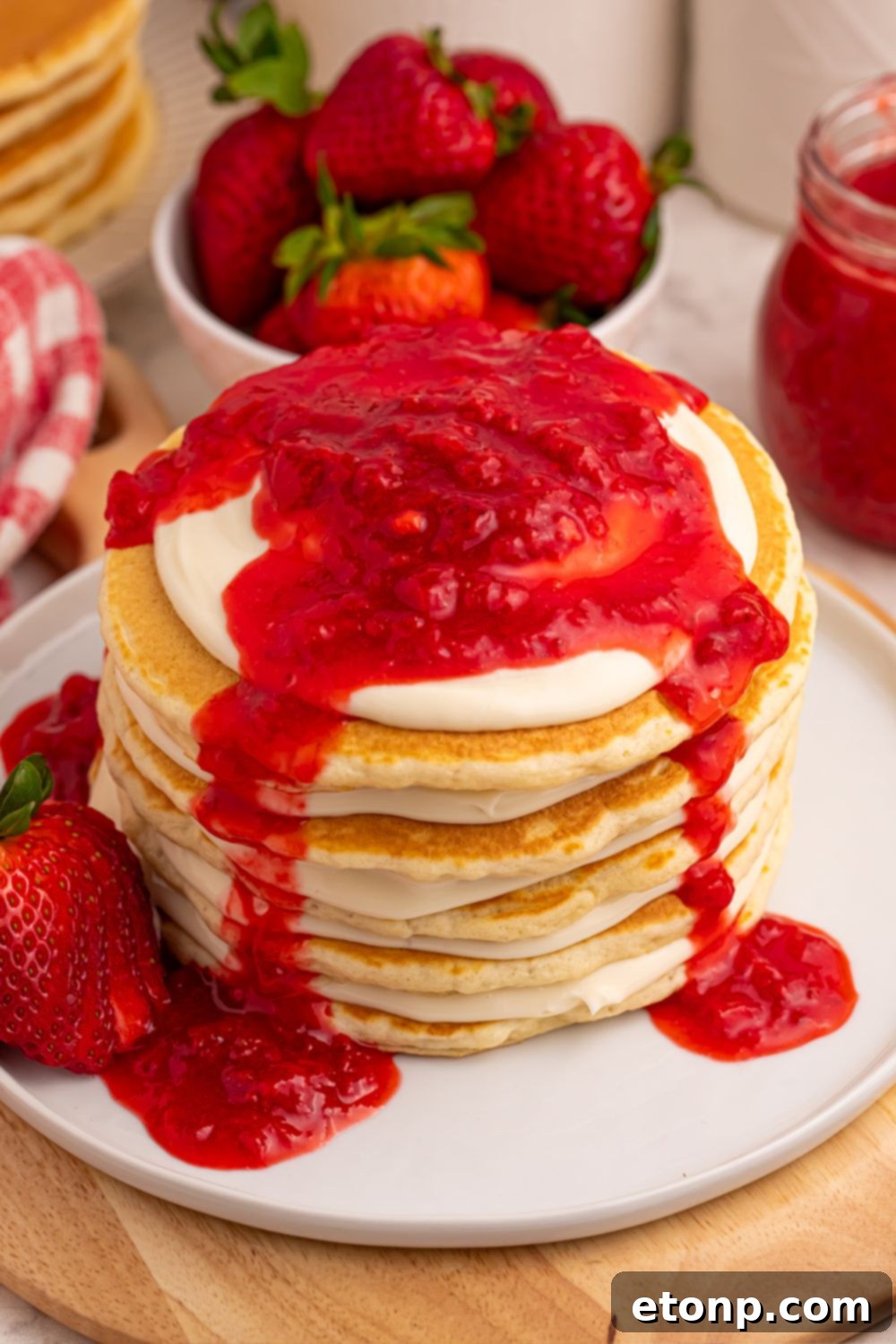 Stacked Strawberry Cheesecake Pancakes on a plate with generous strawberry sauce