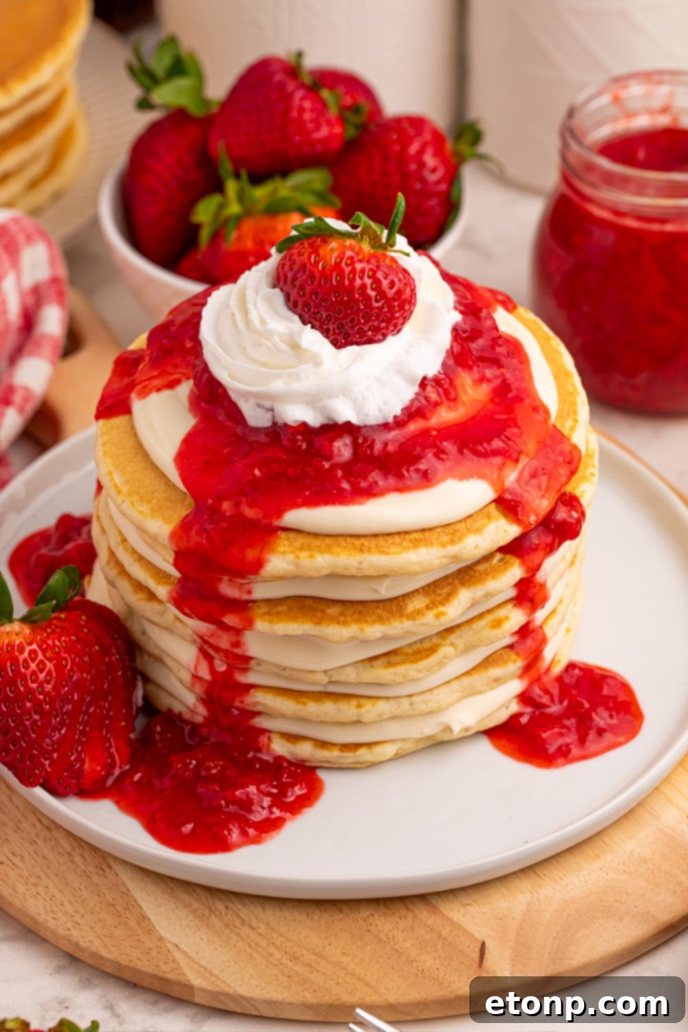 Strawberry Cheesecake Pancakes stacked with whipped cream and berries, with a bowl of berries in the background