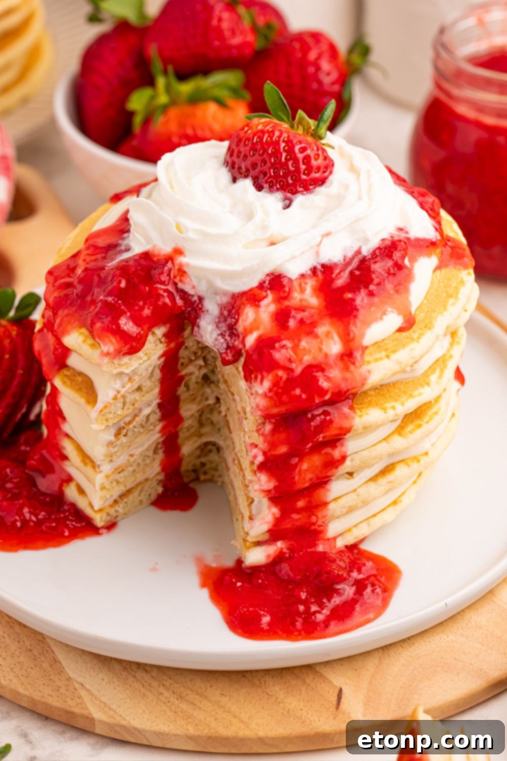 Strawberry Cheesecake Pancakes on a plate with a slice cut out, showing melting whipped cream