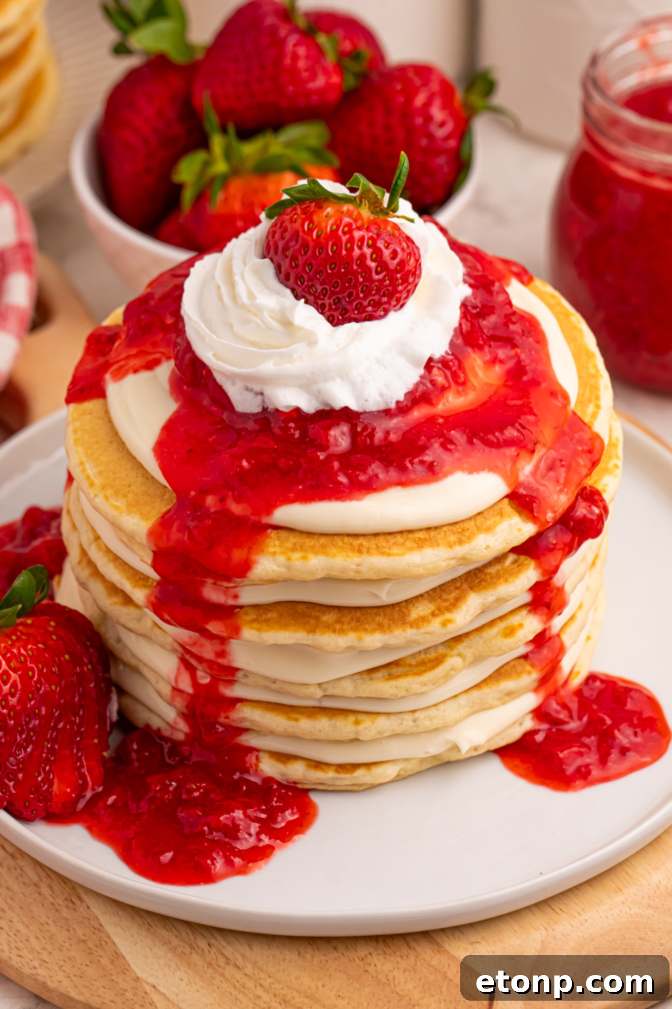 Strawberry Cheesecake Pancakes on a white plate with strawberry sauce drizzled overtop