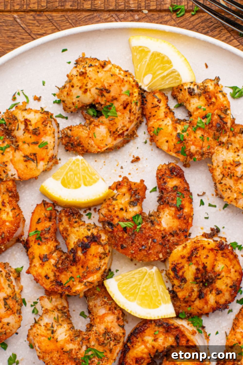 A generous serving of Cajun grilled shrimp, artfully spread out on a white plate with vibrant lemon slices, highlighting the delicious seasoning and perfect cook.